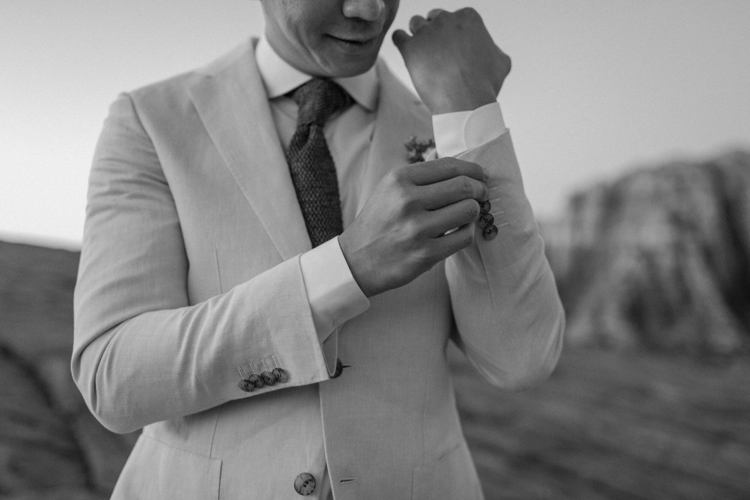 Black and white photo of groom adjusting his cuffs at Snow Canyon State Park in St. George Utah. Utah elopement photographer, Lucy B. Photography. 