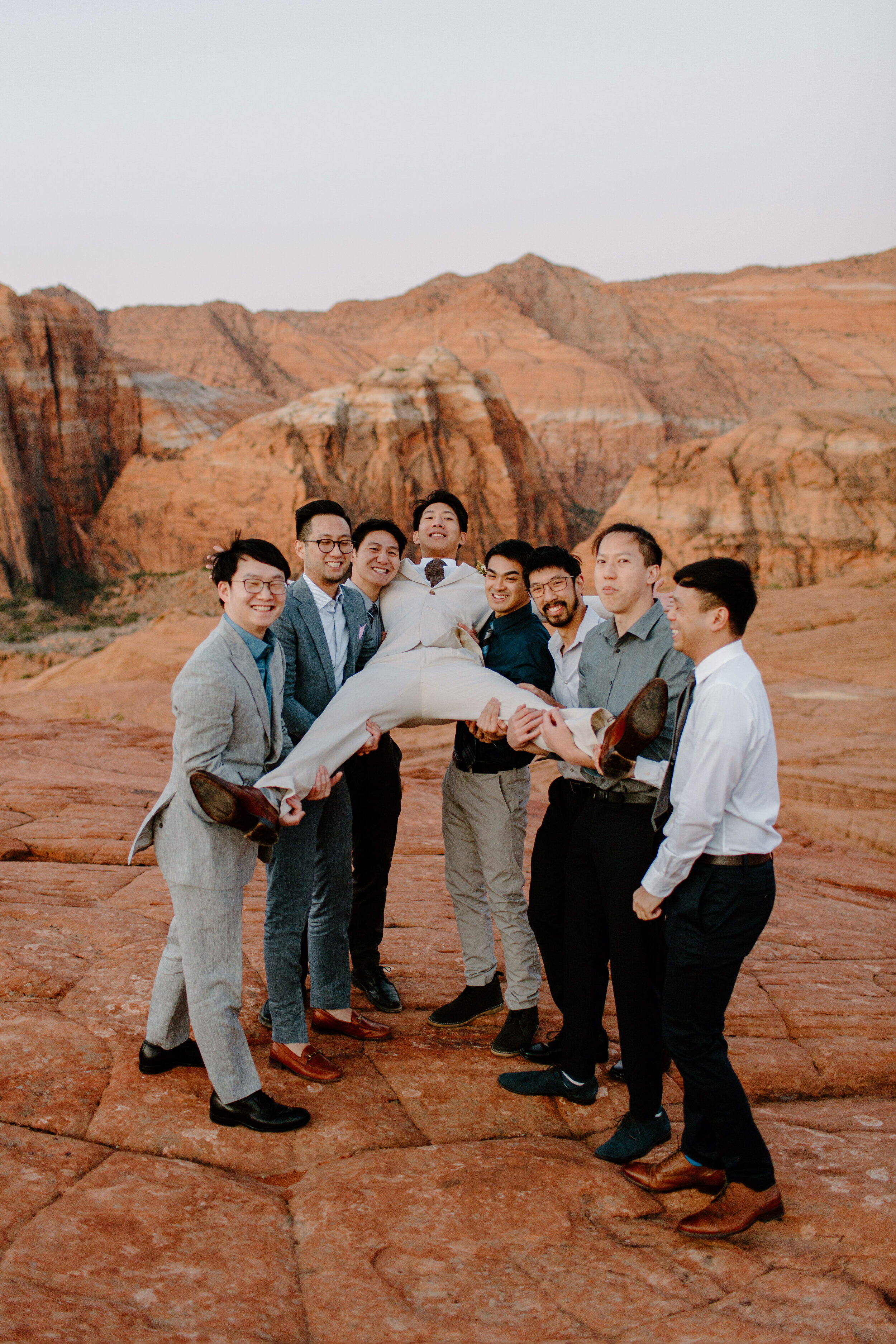  Groom being held off the ground by his groomsmen as they laugh at Snow Canyon State Park in St. George Utah. Utah elopement photographer, Lucy B. Photography. 