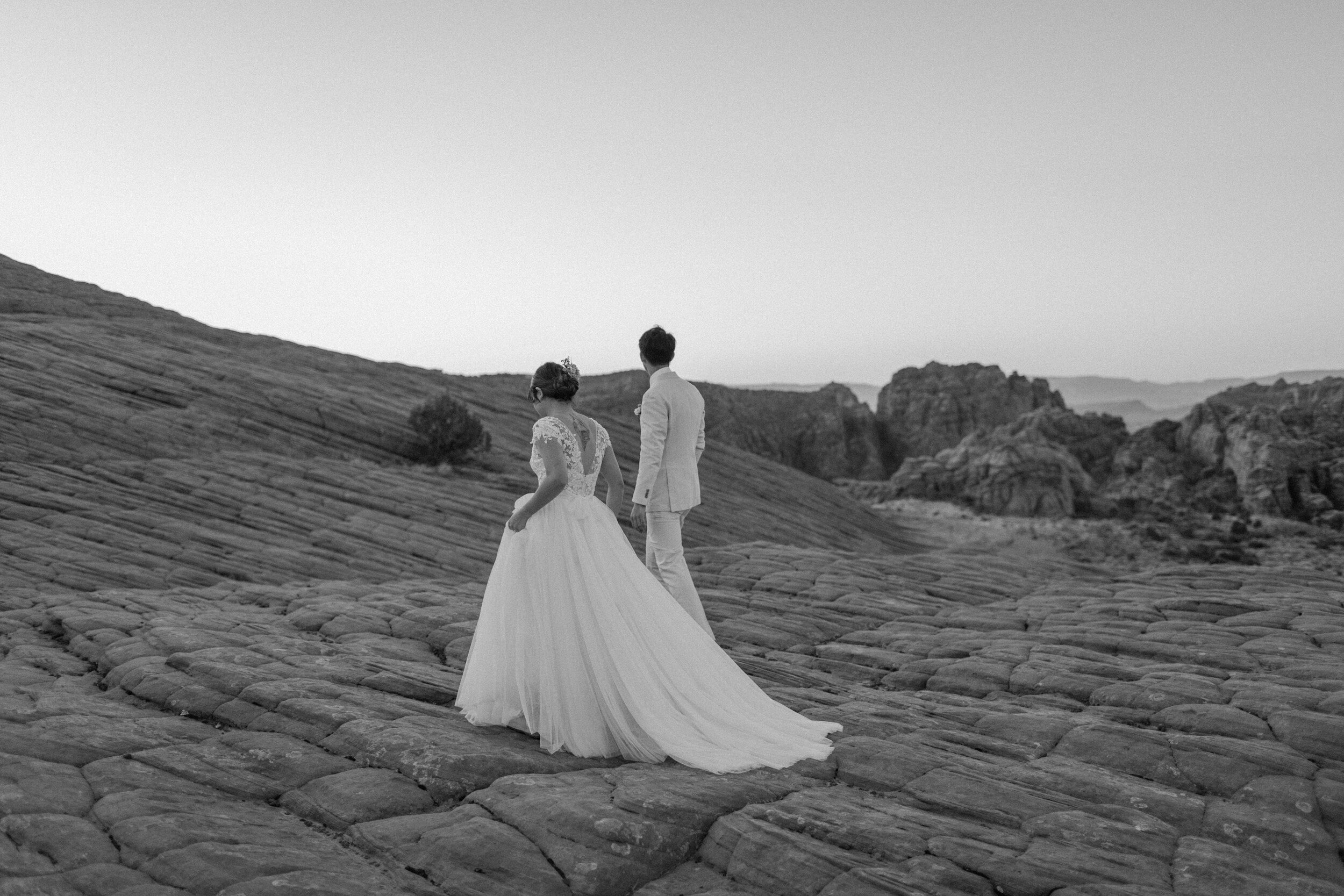  Black and white photo of Utah elopement couple walking away across the red rock landscape at Snow Canyon State Park in St. George Utah. Utah elopement photographer, Lucy B. Photography. 