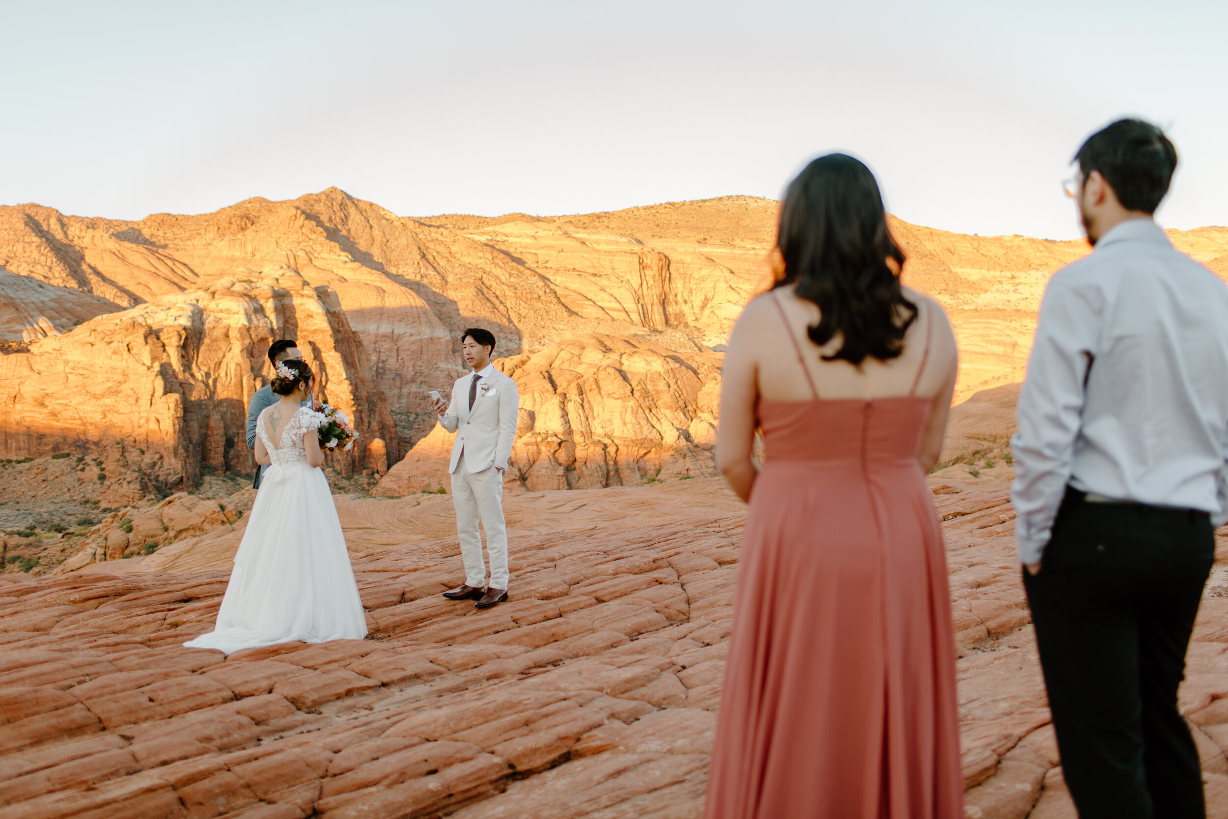  Groom reads his vows to his bride as their friends look on during their Utah elopement at Snow Canyon State Park in St. George Utah. Utah elopement photographer, Lucy B. Photography. 