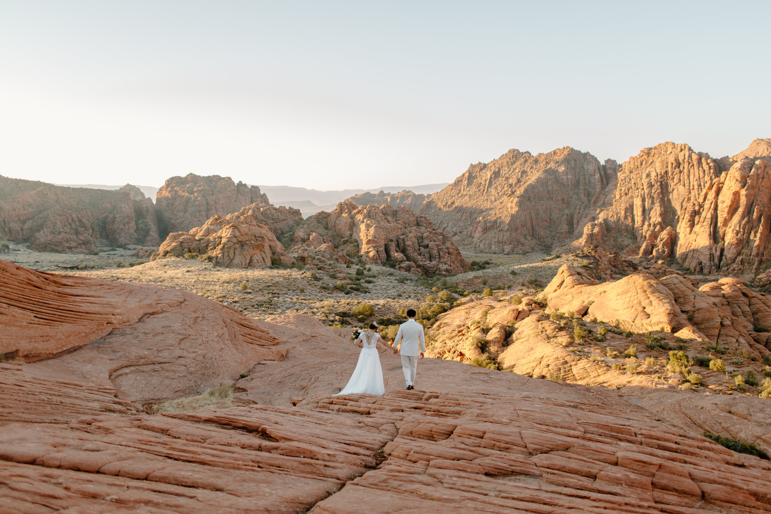  Wide shot of Utah elopement couple walking away into the red rock landscape at Snow Canyon State Park in St. George Utah. Utah elopement photographer, Lucy B. Photography. 