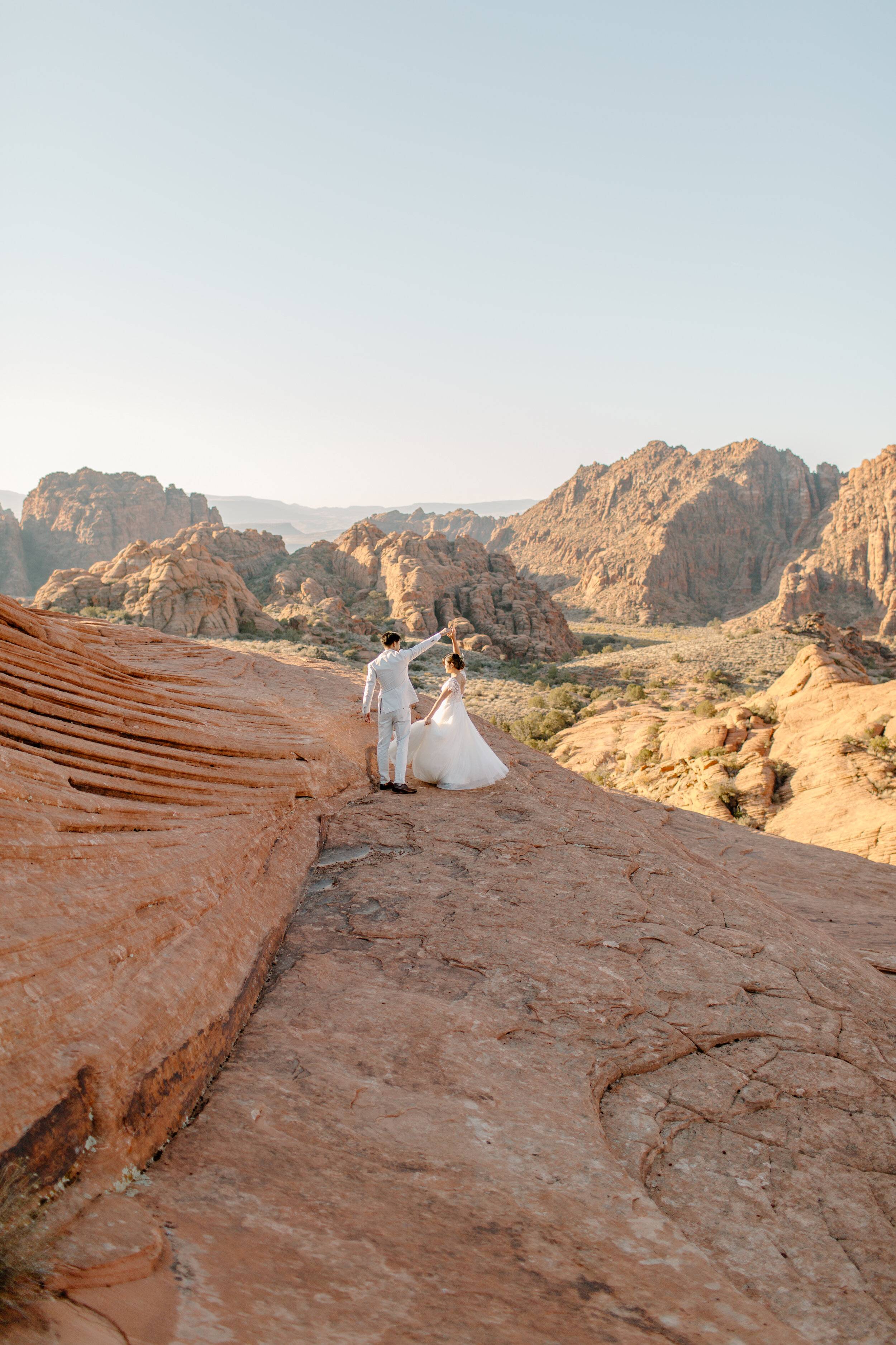  Wide shot of Utah elopement couple dancing in a red rock landscape, the dress flying in the air at Snow Canyon State Park in St. George Utah. Utah elopement photographer, Lucy B. Photography. 