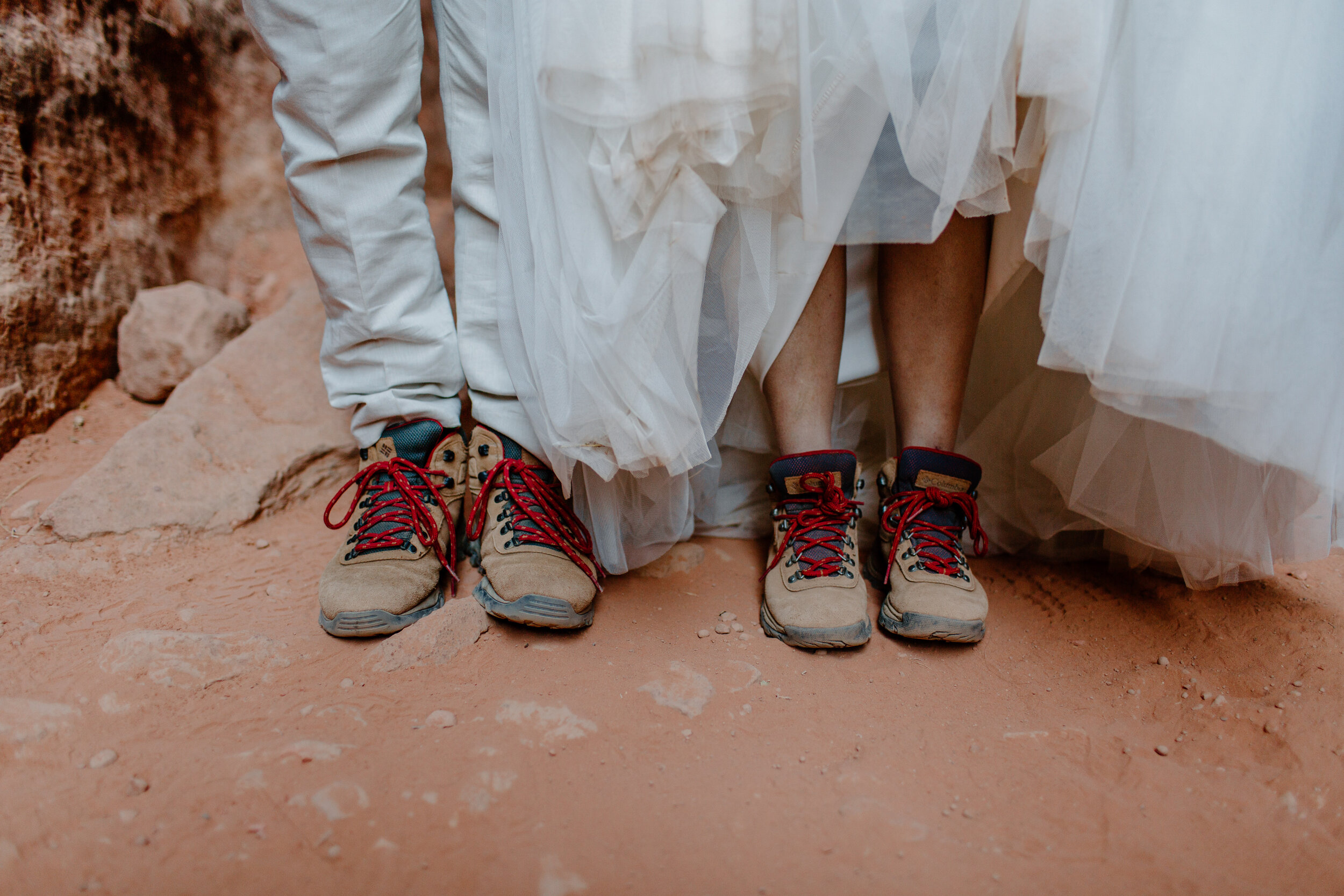  Close up photo of Utah elopement couple’s legs while they are wearing matching hiking boots with their formal clothes at Snow Canyon State Park in St. George Utah. Utah elopement photographer, Lucy B. Photography. 