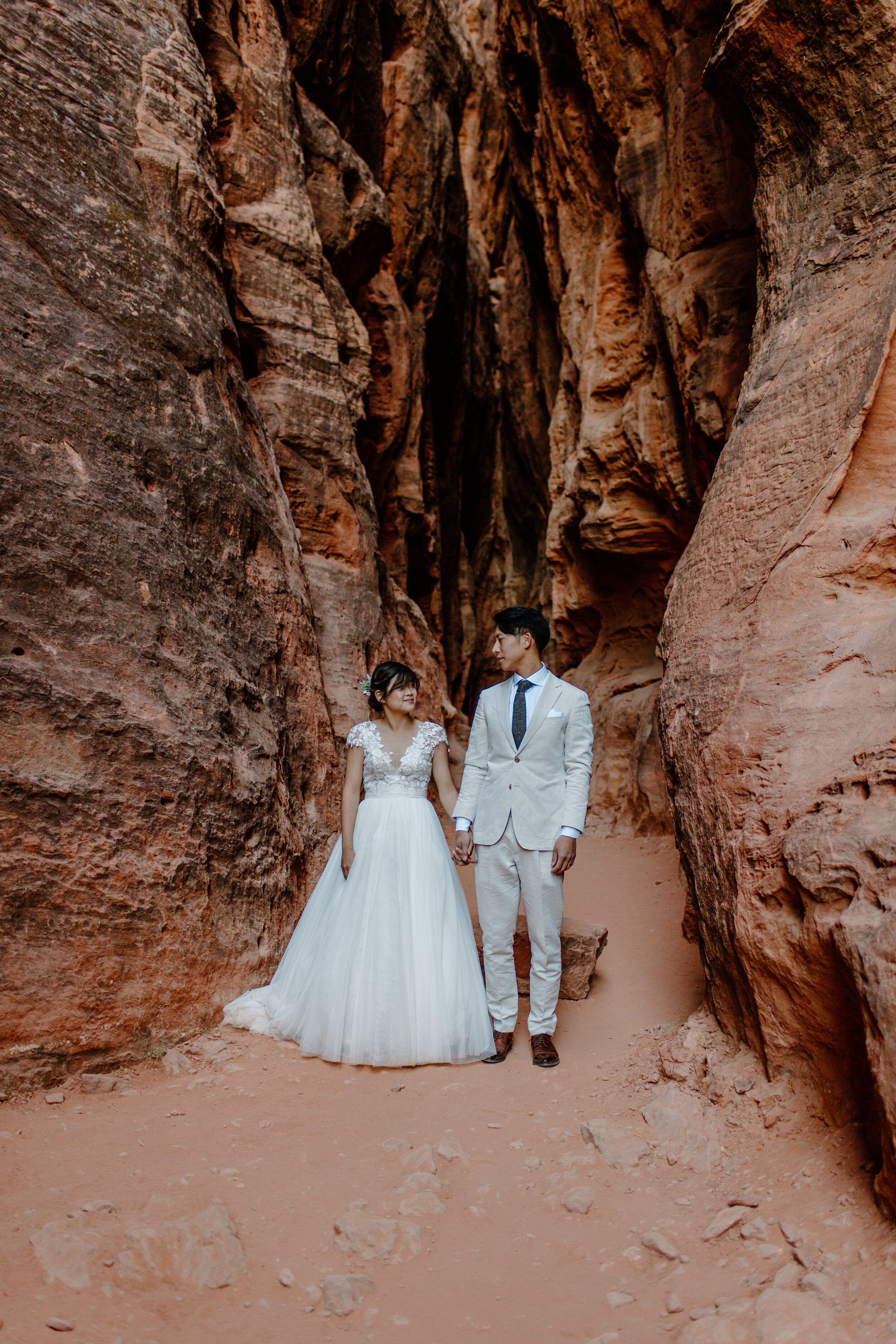  Utah elopement couple hold hands and look at each other in the middle of a slot canyon at Snow Canyon State Park in St. George Utah. Utah elopement photographer, Lucy B. Photography. 
