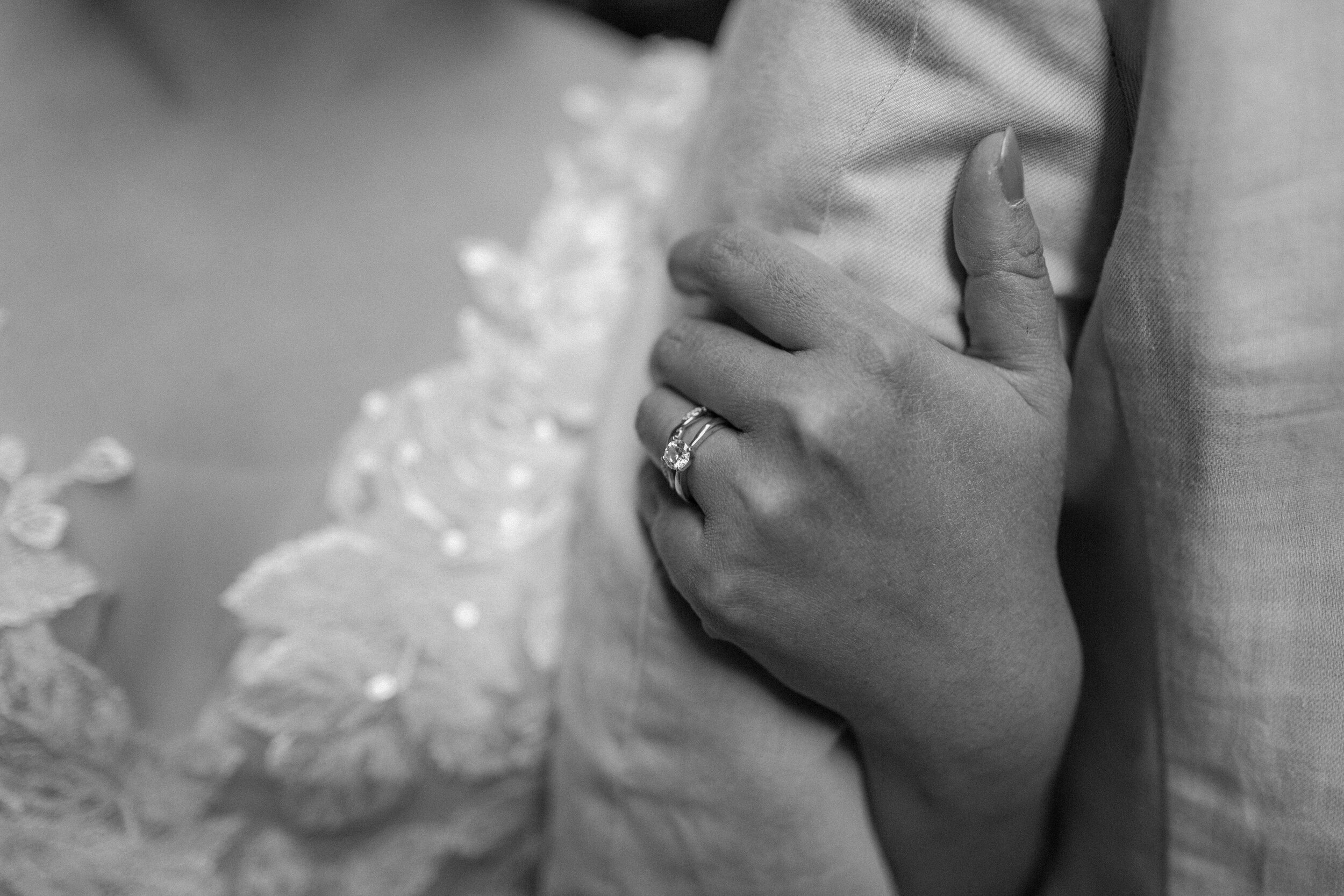  Black and white close up photo of a bride showing off her wedding ring while holding her husband’s arm at Snow Canyon State Park in St. George Utah. Utah elopement photographer, Lucy B. Photography. 
