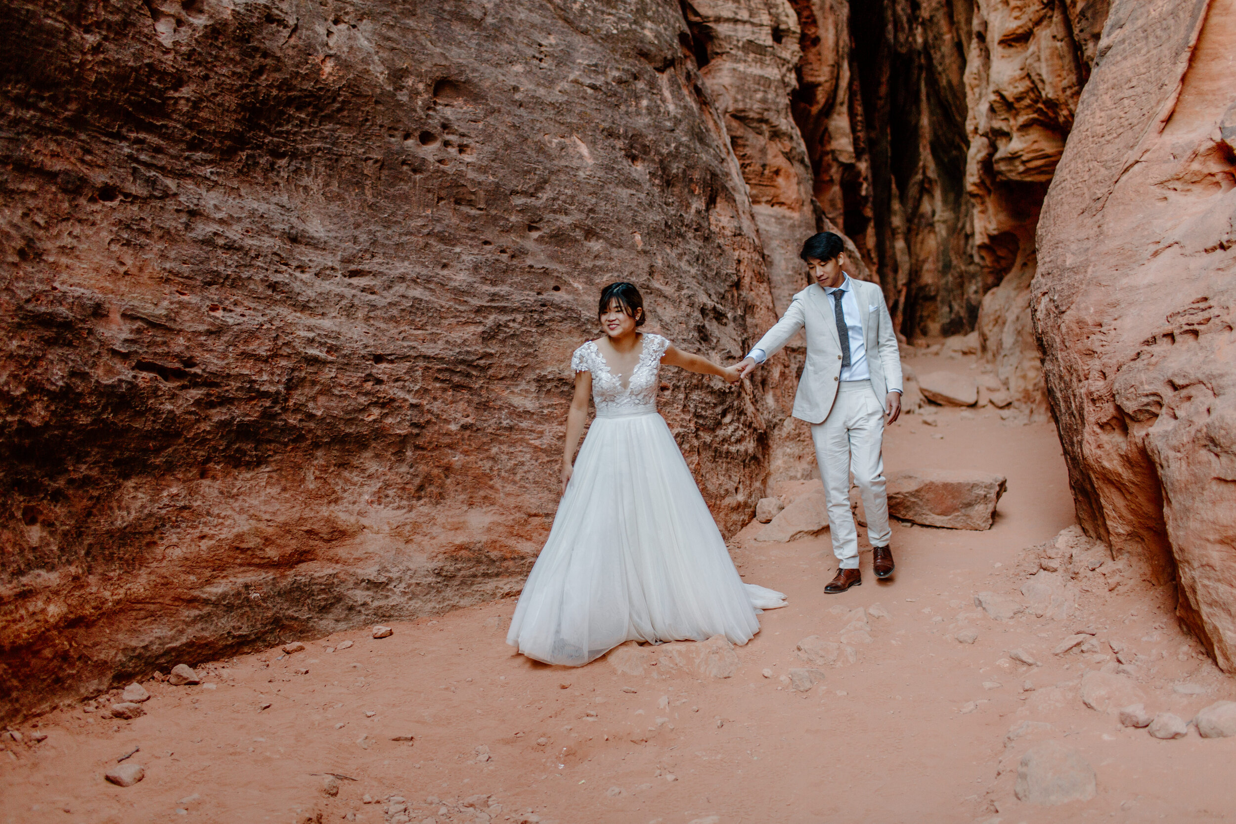  Utah elopement bride leads her groom by the hand through a slot canyon at Snow Canyon State Park in St. George Utah. Utah elopement photographer, Lucy B. Photography. 