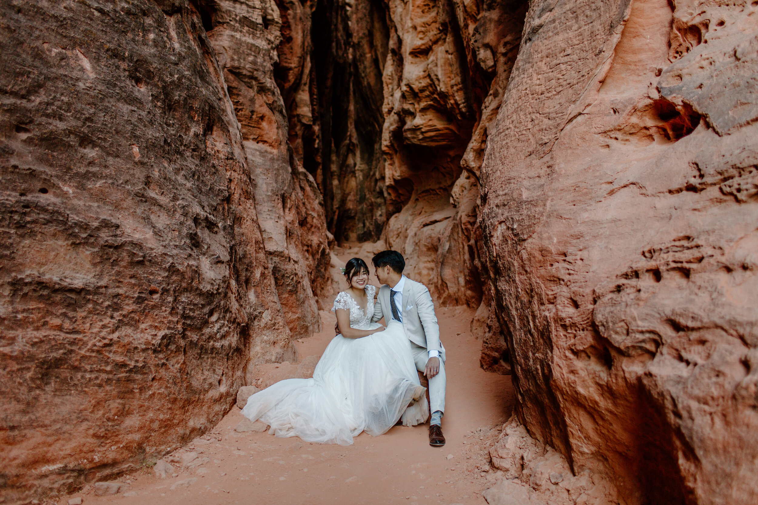  Utah elopement couple sits on a rock in the middle of a slot canyon and laughs together at Snow Canyon State Park in St. George Utah. Utah elopement photographer, Lucy B. Photography. 