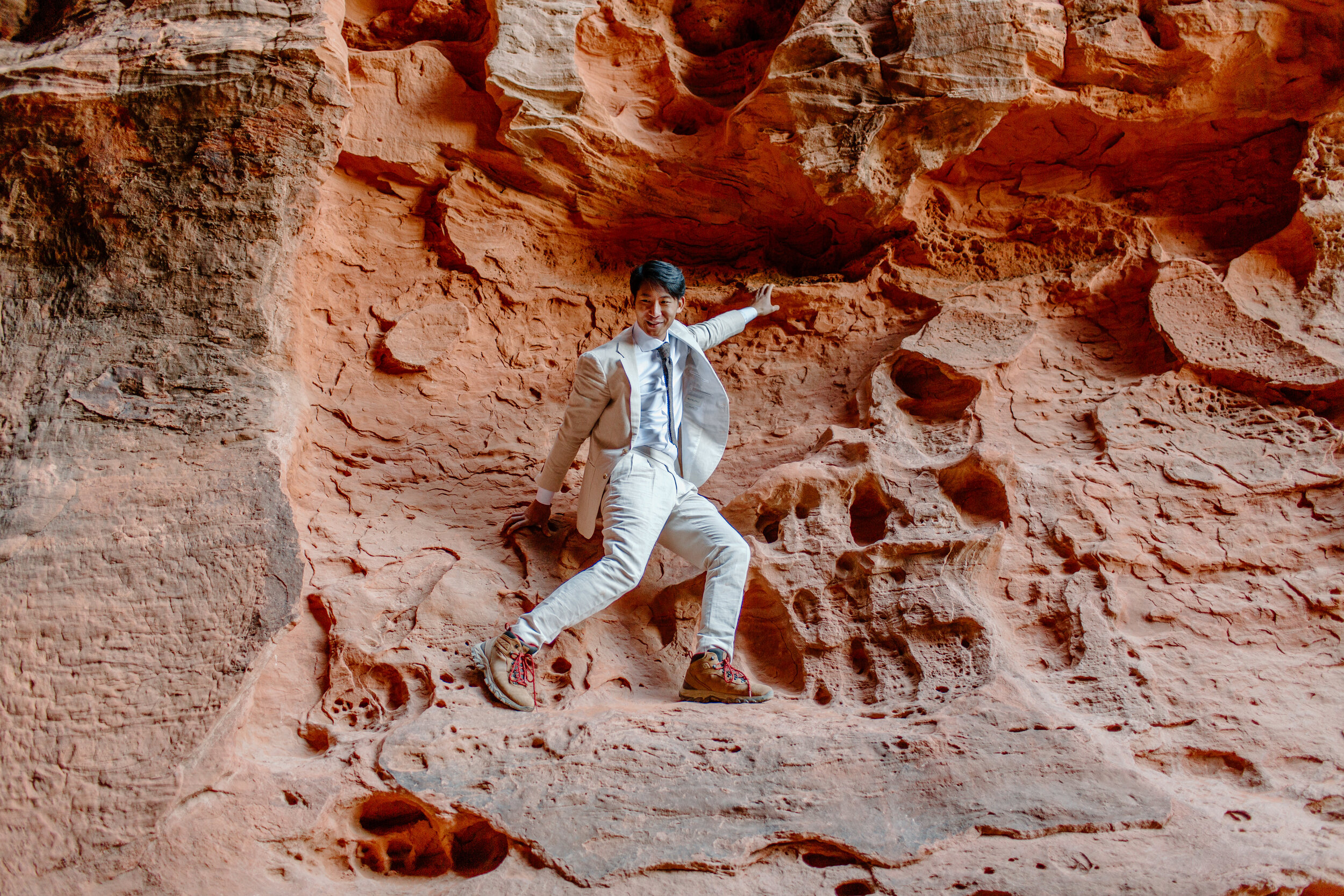  Utah elopement groom stands on the wall of a slot canyon after climbing up it at Snow Canyon State Park in St. George Utah. Utah elopement photographer, Lucy B. Photography. 