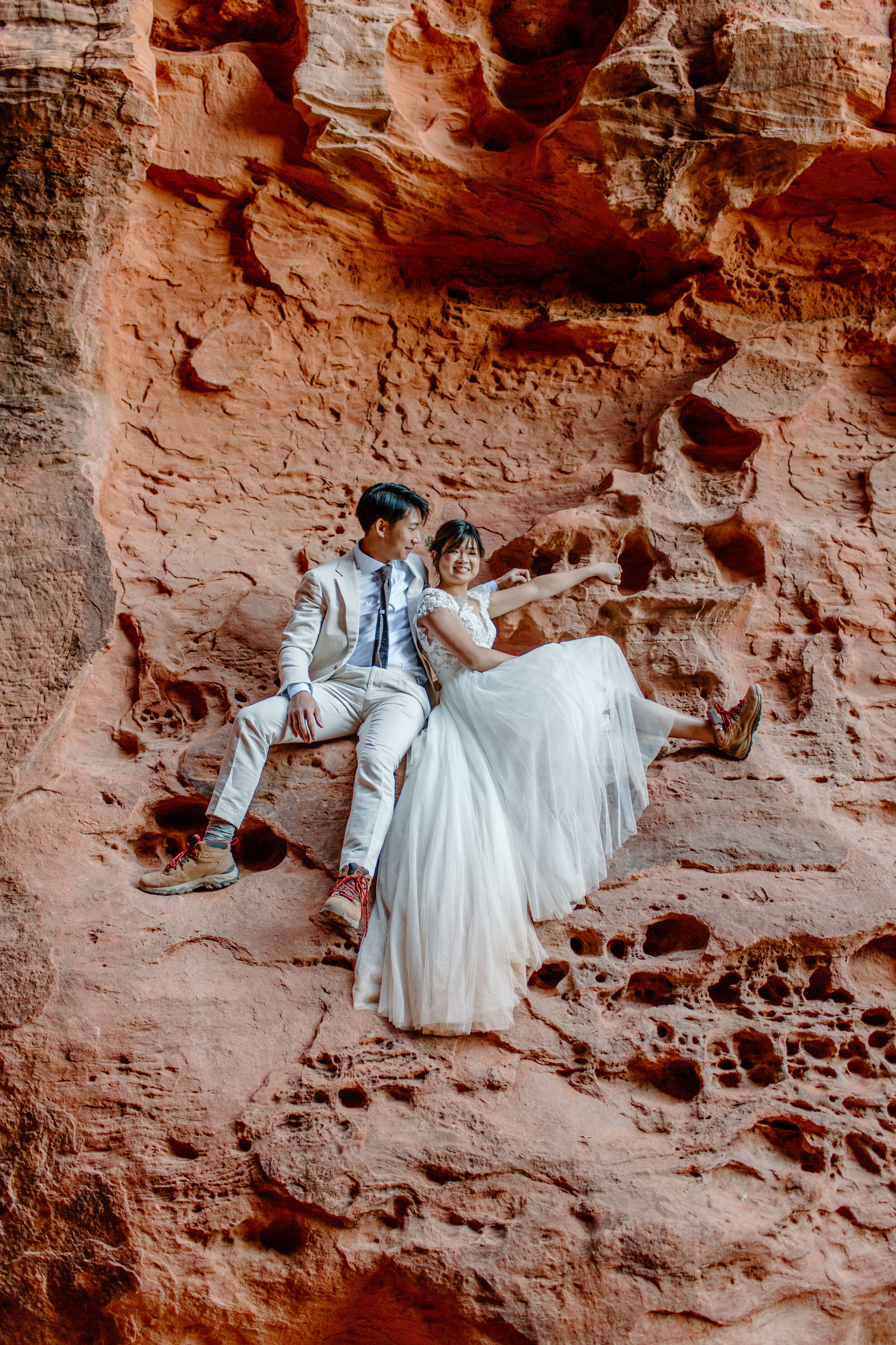  Utah elopement couple cuddles while sitting on a ledge on the side of a slot canyon after climbing up at Snow Canyon State Park in St. George Utah. Utah elopement photographer, Lucy B. Photography. 