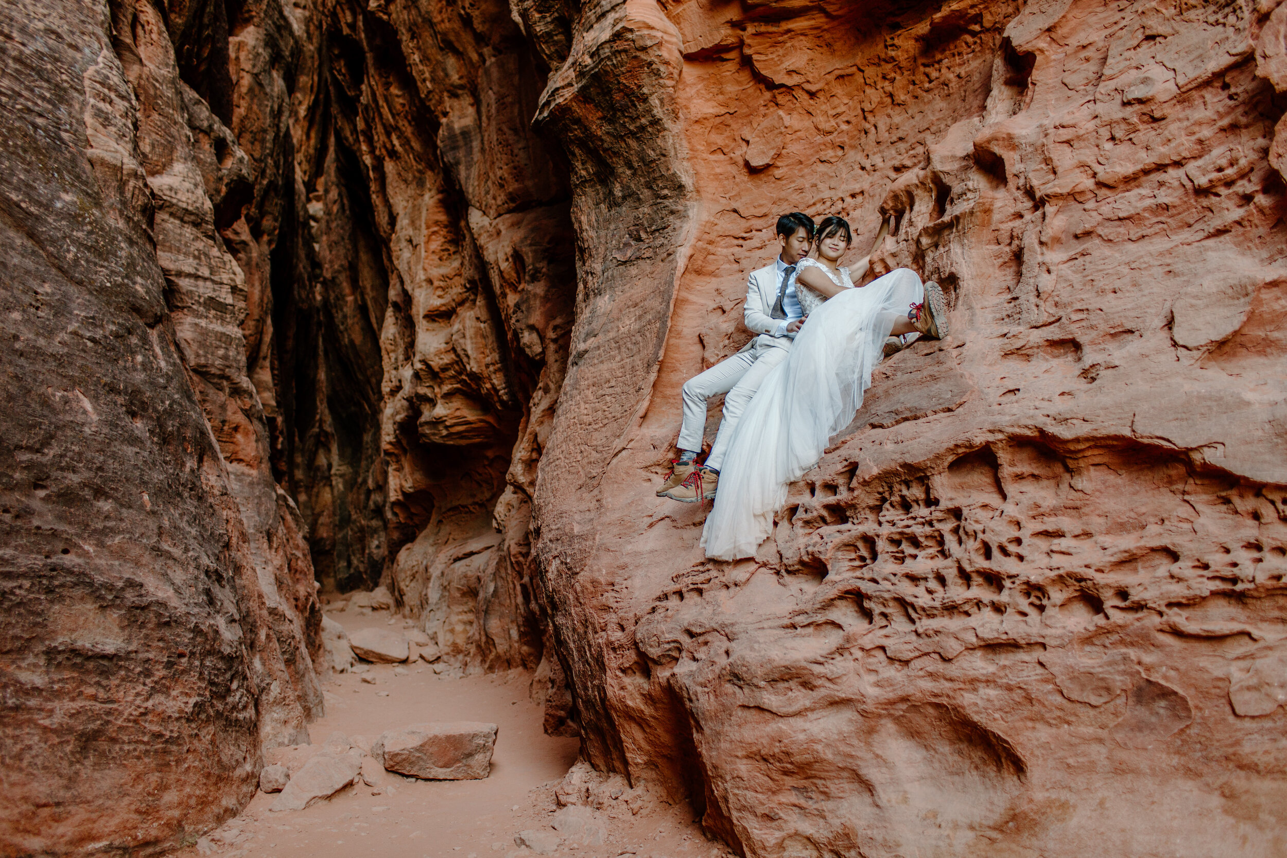  Utah elopement couple cuddles on a ledge on the wall of a slot canyon at Snow Canyon State Park in St. George Utah. Utah elopement photographer, Lucy B. Photography. 