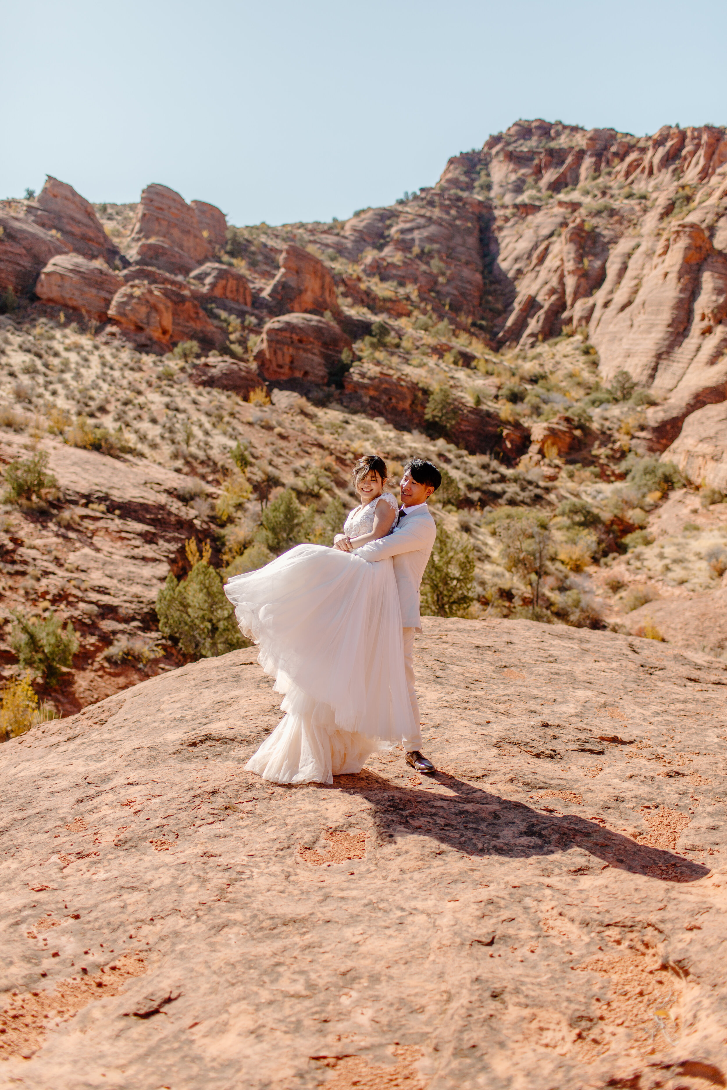  Utah elopement groom holds his wife and spins her around sending her dress flying in St. George Utah. Utah elopement photographer, Lucy B. Photography. 