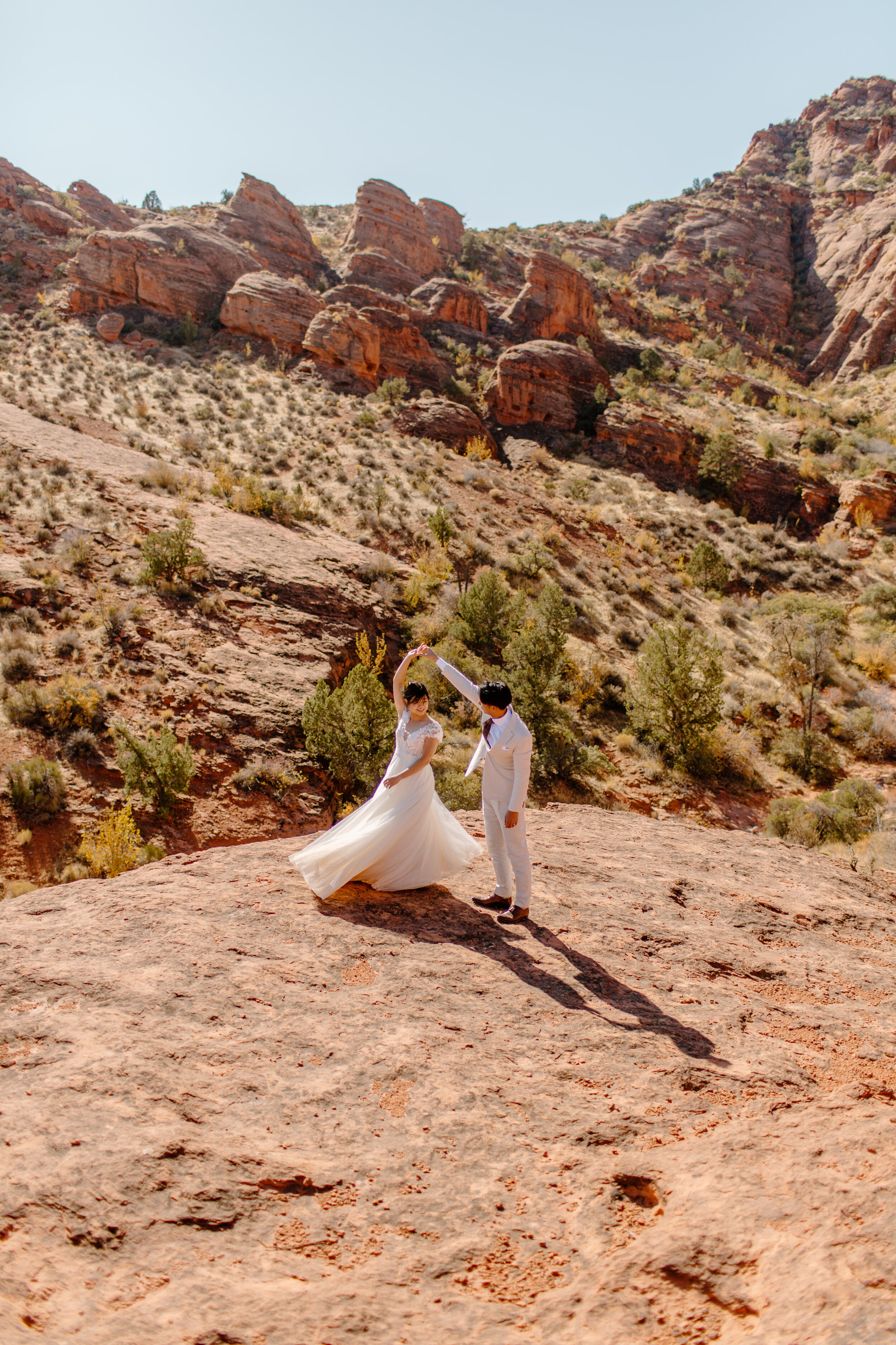  Wide shot of a Utah elopement couple dancing and spinning around in front of a mountain landscape in St. George Utah. Utah elopement photographer, Lucy B. Photography. 