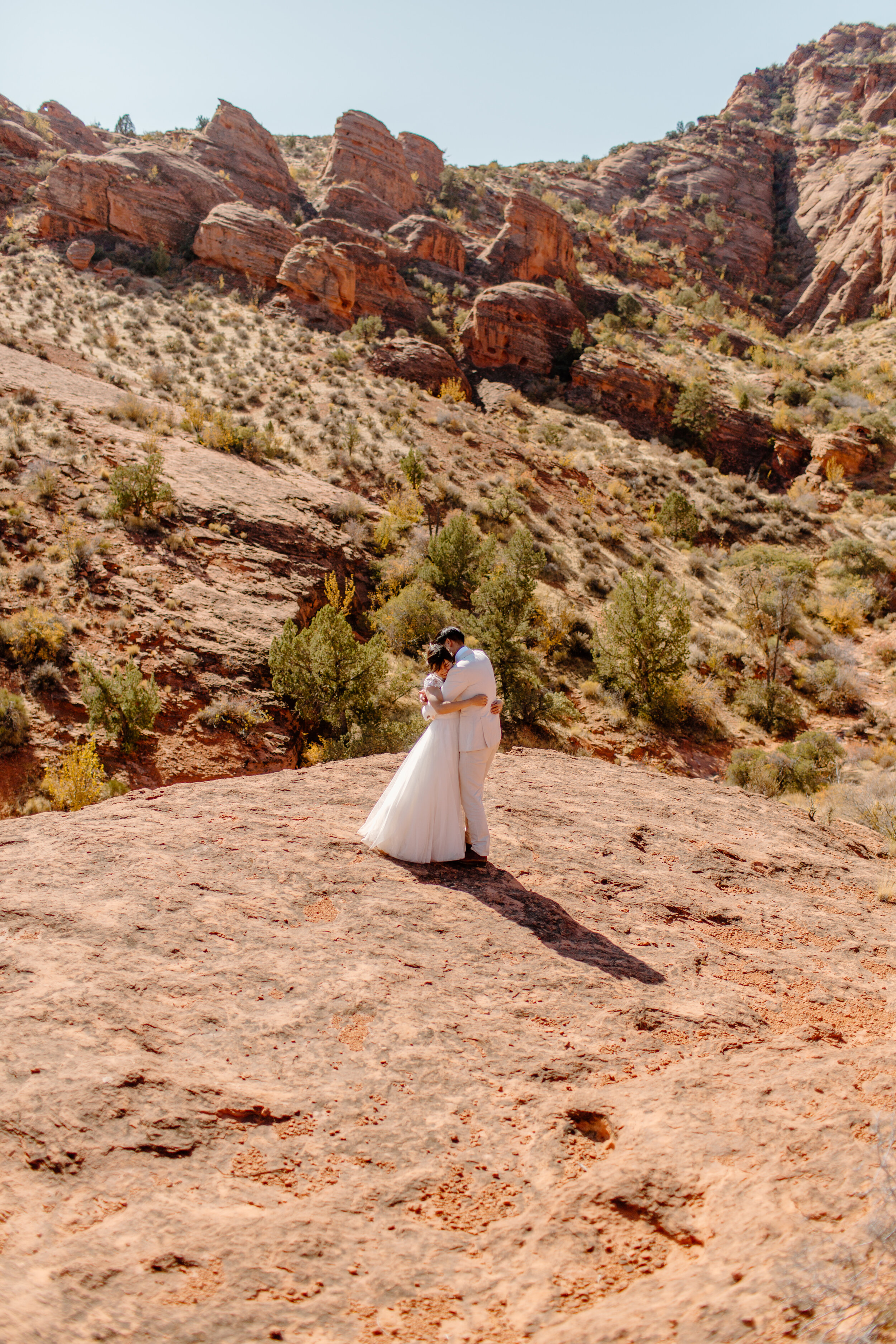  Wide shot of Utah elopement couple hugging each other in front of a mountain landscape in St. George Utah. Utah elopement photographer, Lucy B. Photography. 