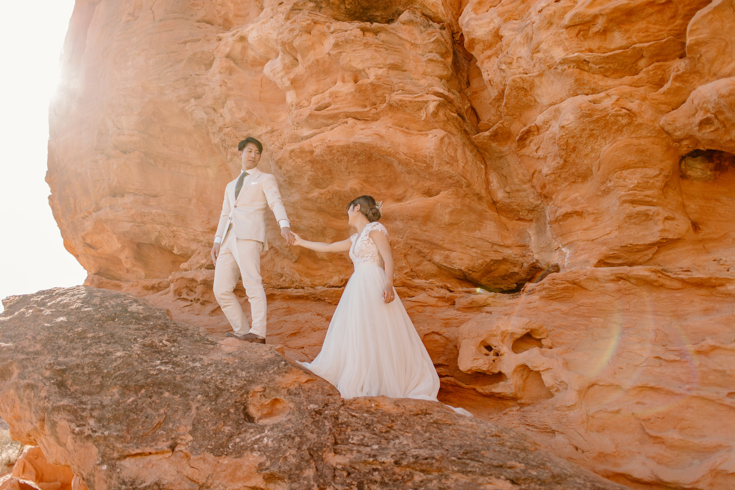  Utah elopement couple walks together up a ledge on a wall of red rock in St. George Utah. Utah elopement photographer, Lucy B. Photography. 