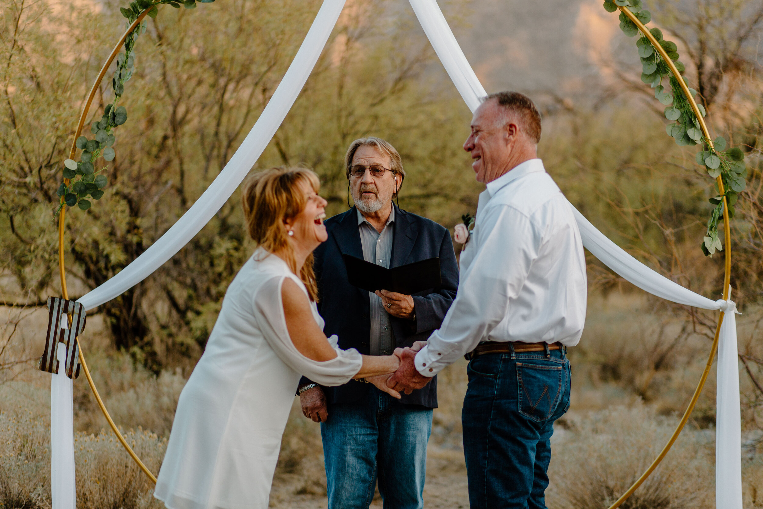  Elopement couple holds hands and laughs together at their officiant’s speech in Catalina State Park in Tucson. Tucson elopement photographer, Lucy B. Photography. 