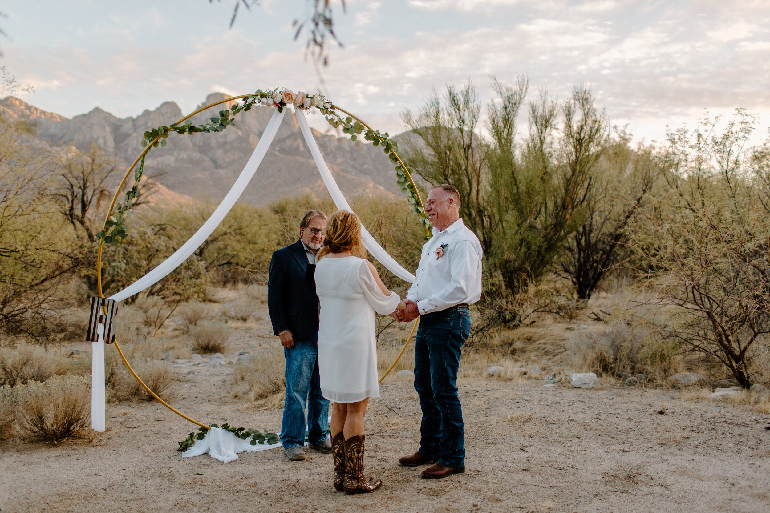  Elopement couple holds hands in front of their arch with a mountain backdrop in Catalina State Park in Tucson. Tucson elopement photographer, Lucy B. Photography. 