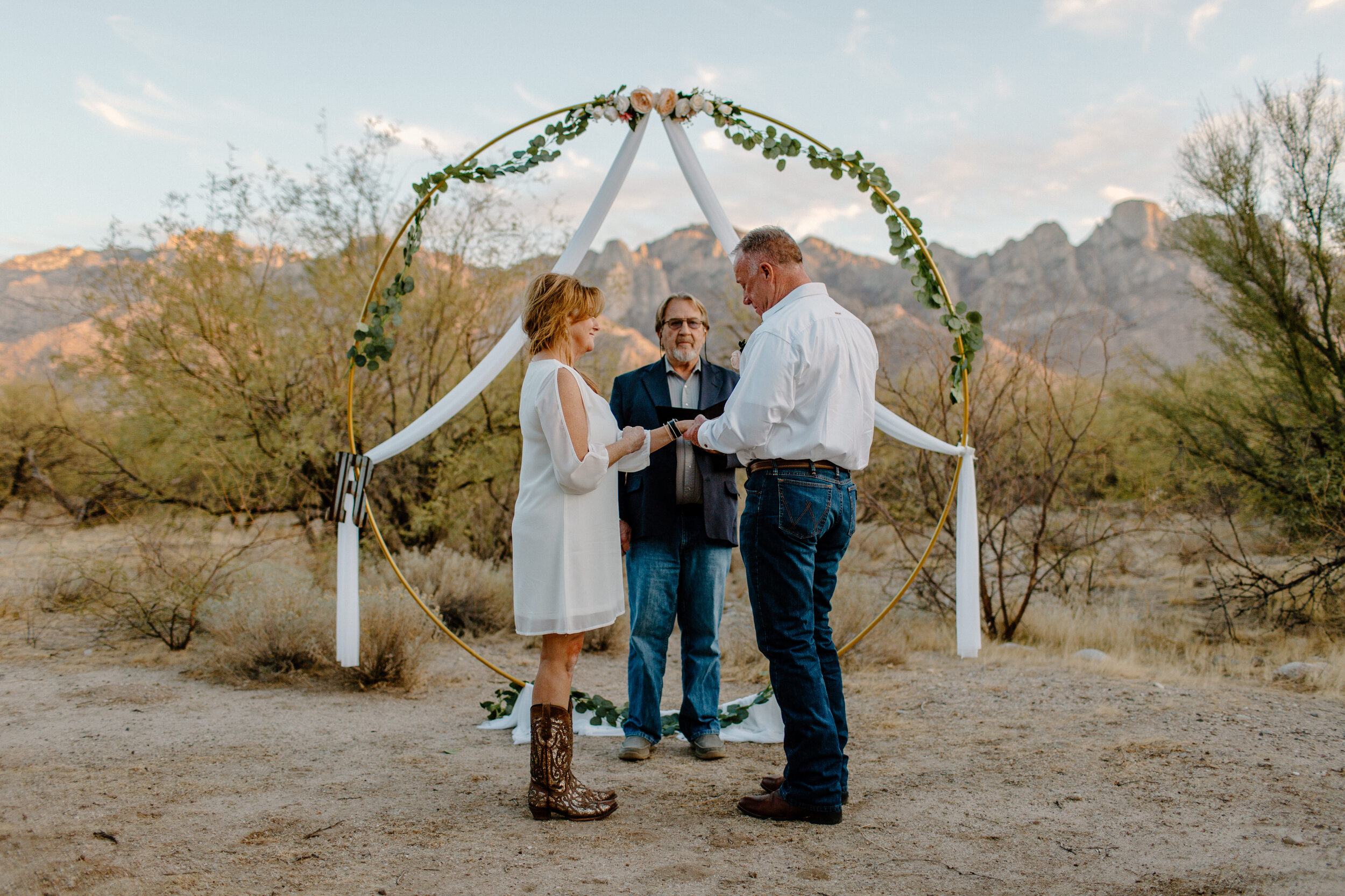  Groom puts a wedding band on his bride’s finger in front of a mountain backdrop in Catalina State Park in Tucson. Tucson elopement photographer, Lucy B. Photography. 
