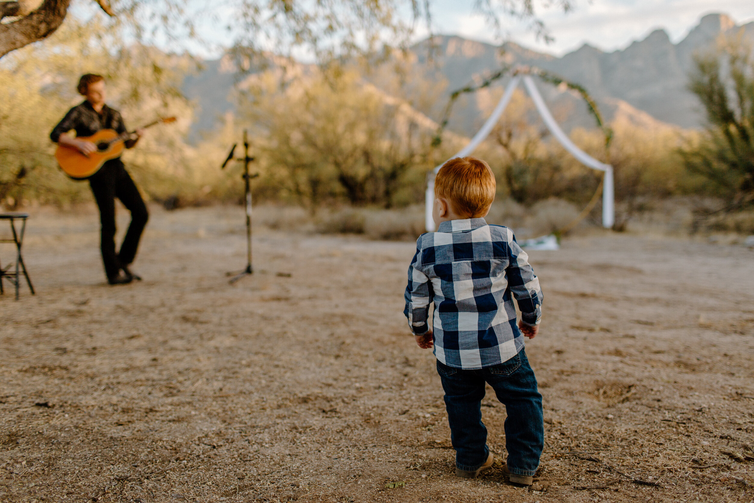  Small toddler watches a man play guitar and sing before an elopement in Catalina State Park in Tucson. Tucson elopement photographer, Lucy B. Photography. 