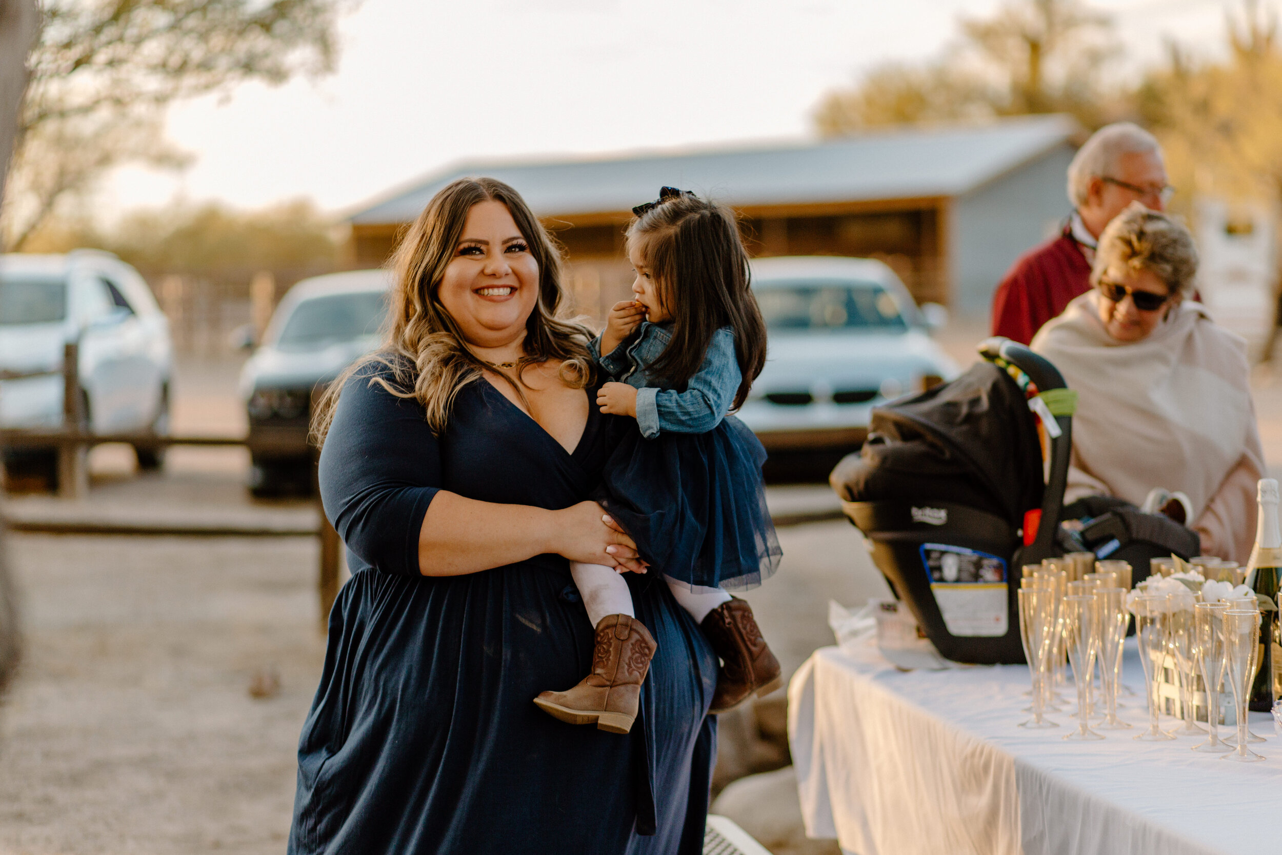  Woman smiles at camera while holding her toddler daughter as they wait for the woman’s parents to arrive for their elopement in Catalina State Park in Tucson. Tucson elopement photographer, Lucy B. Photography. 
