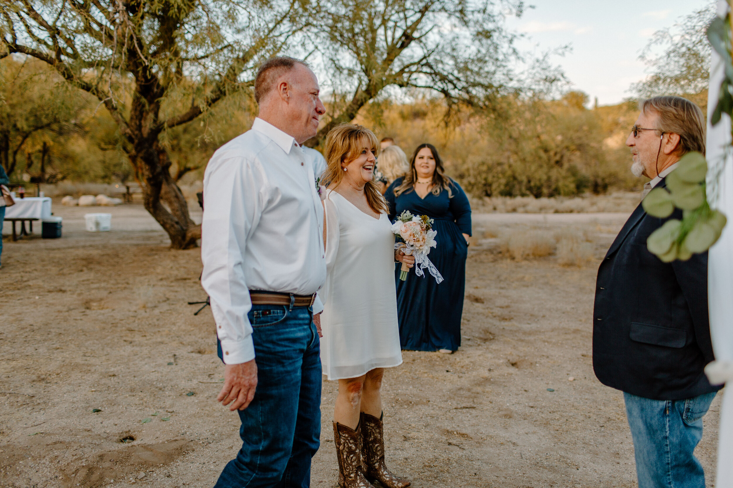  Elopement couple smiles and walks up to their ceremony spot as their family watches in Catalina State Park in Tucson. Tucson elopement photographer, Lucy B. Photography. 