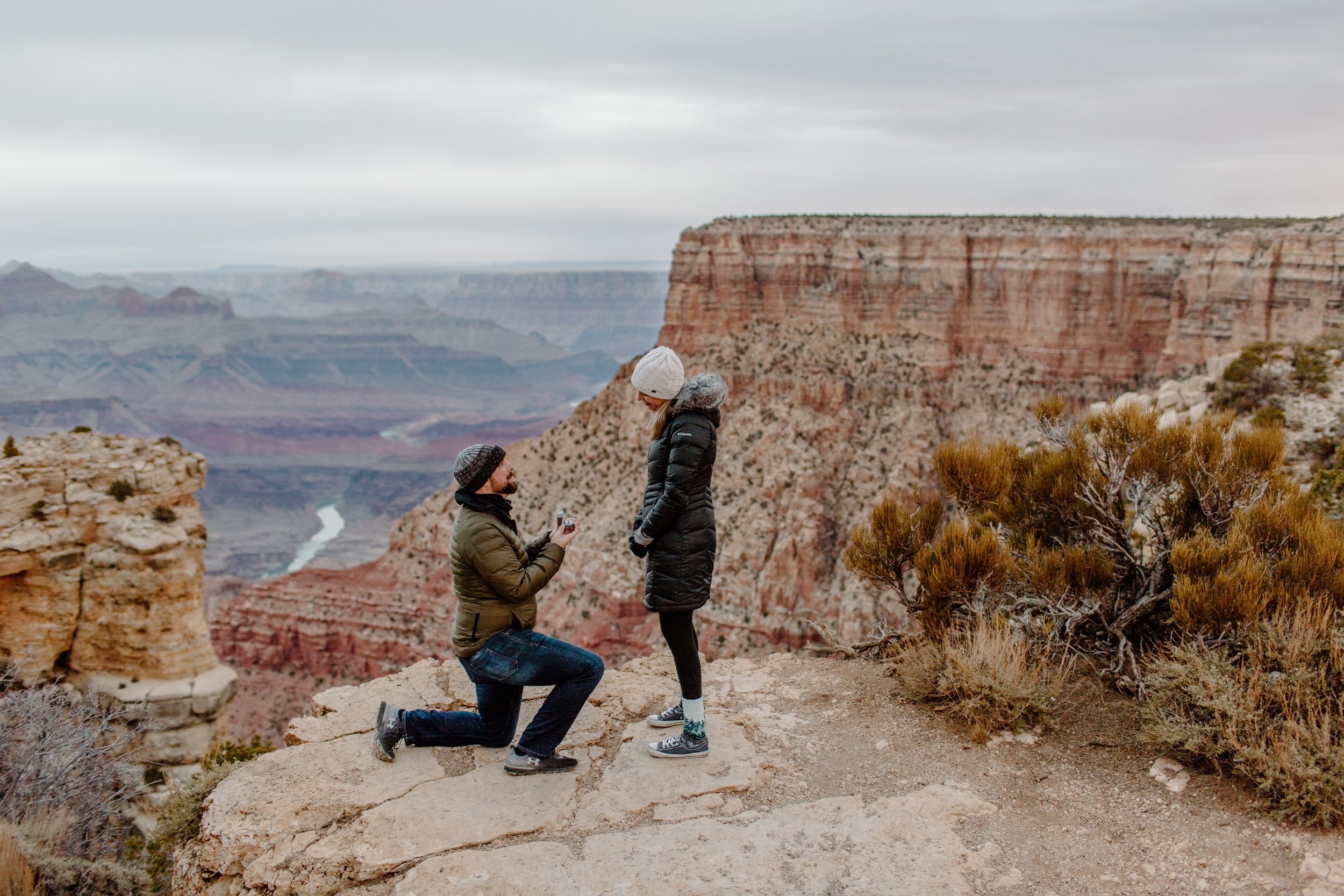  Man proposes to his girlfriend at the edge of the Grand Canyon with the Colorado River in the background 