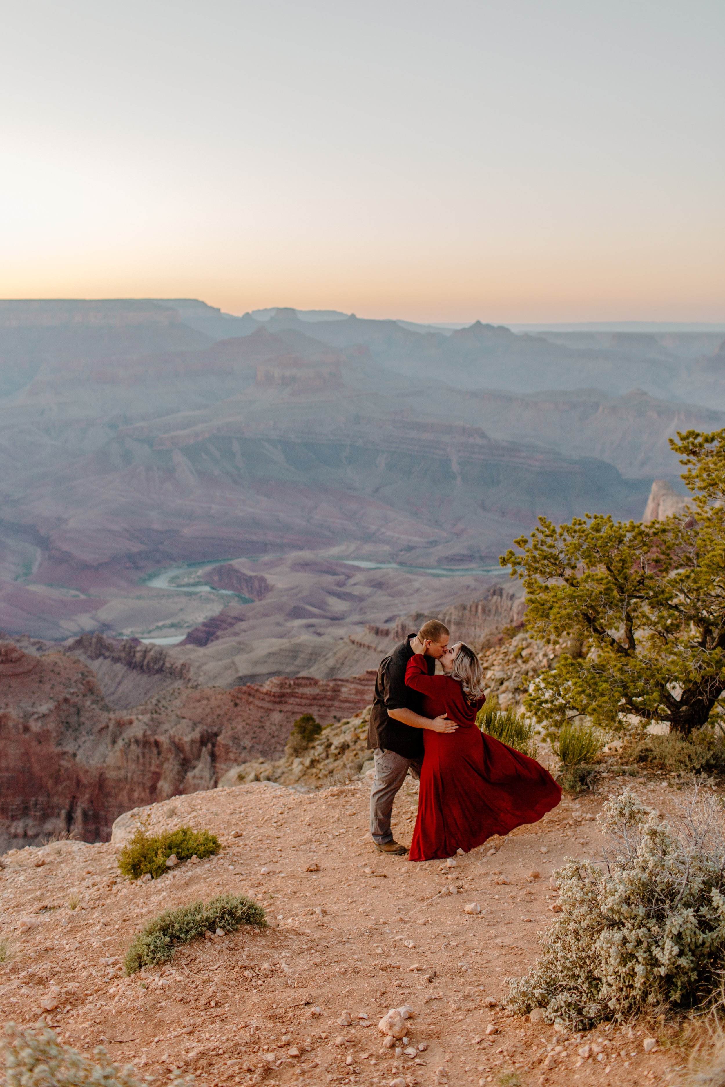  Couple kisses at the edge of the Grand Canyon at sunset and woman throws her dress back in the wind 