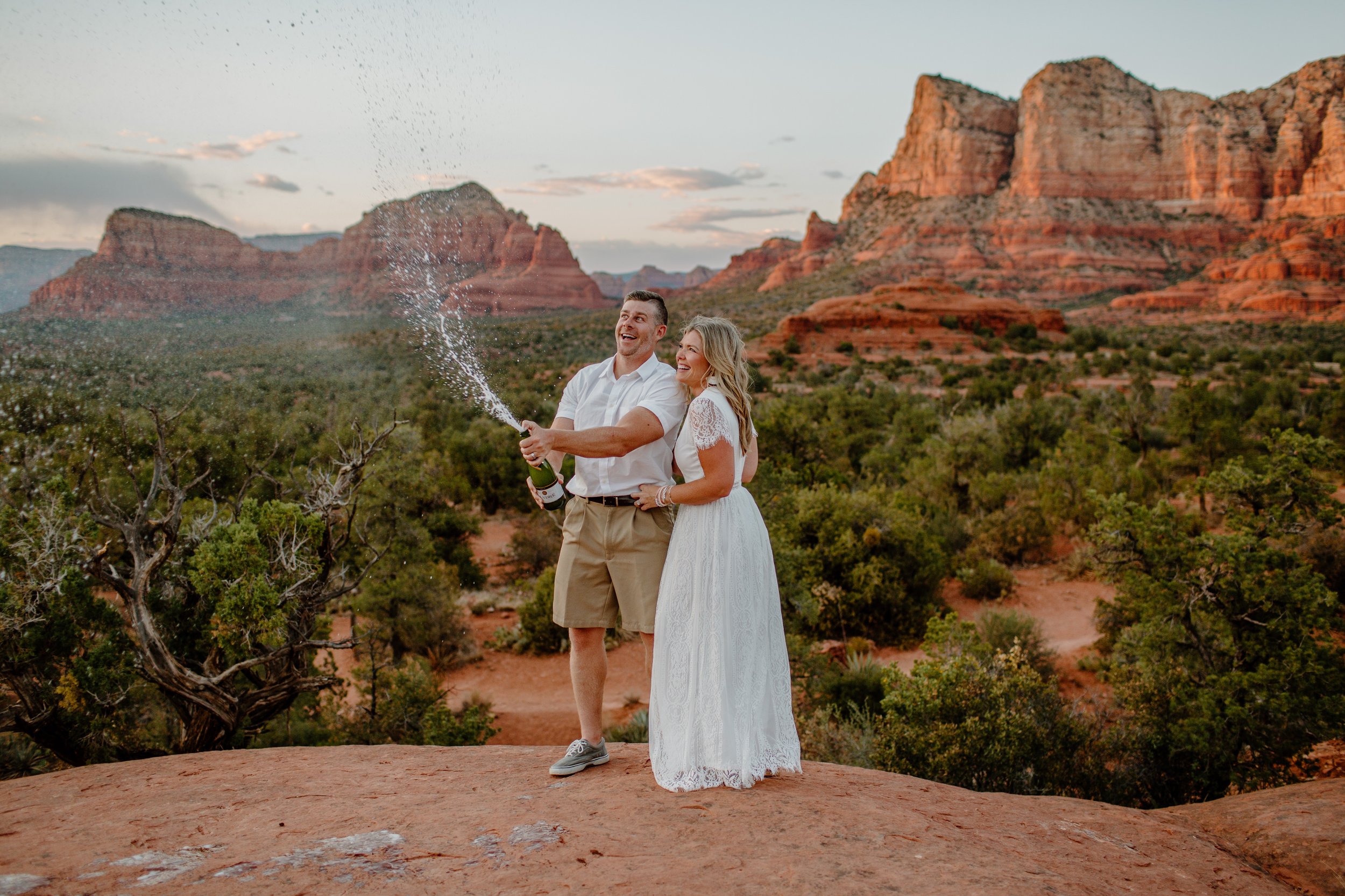  Couple sprays a bottle of champagne with mountains in the background at Bell Rock in Sedona 