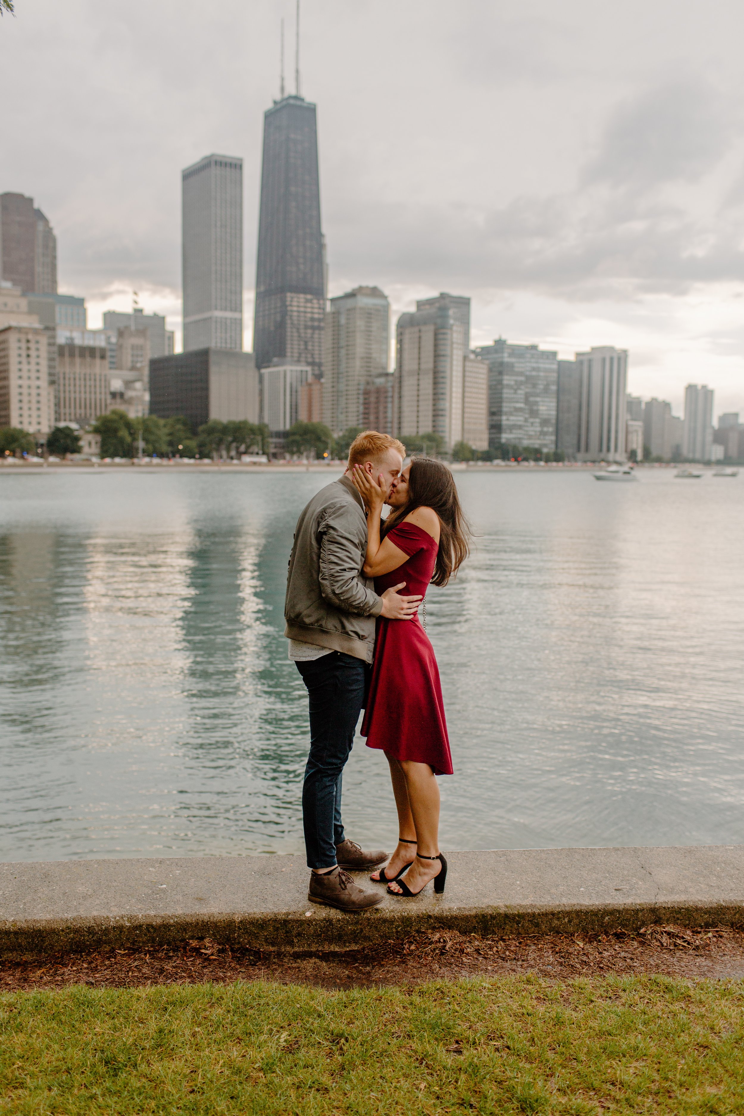  Couple kisses passionately after proposal in front of Chicago skyline at Olive Park 