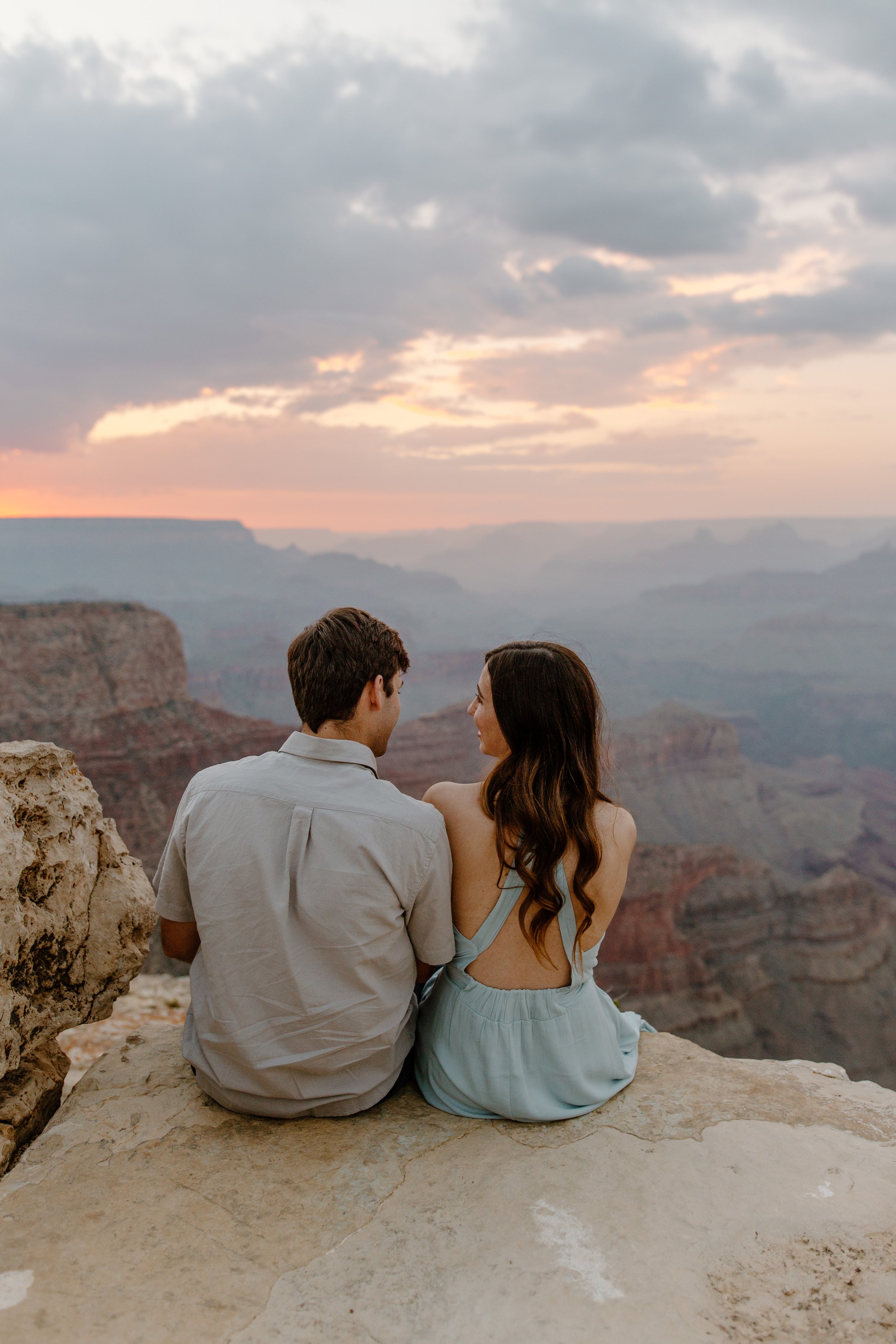 Couple sitting at the edge of the Grand Canyon at sunset and looking at each other 