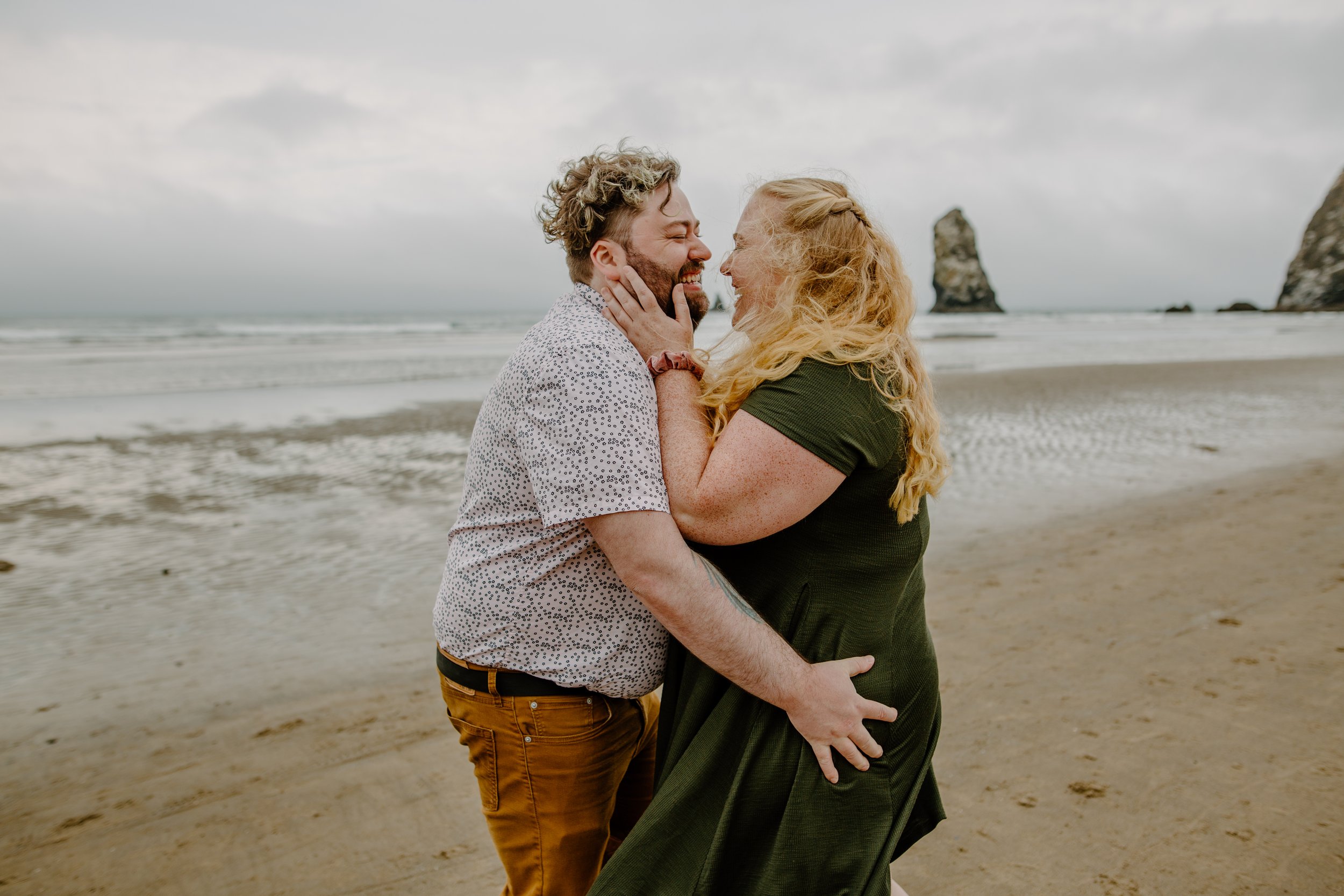  Couple holds each other and laughs in front of Haystack Rock in Cannon Beach Oregon 