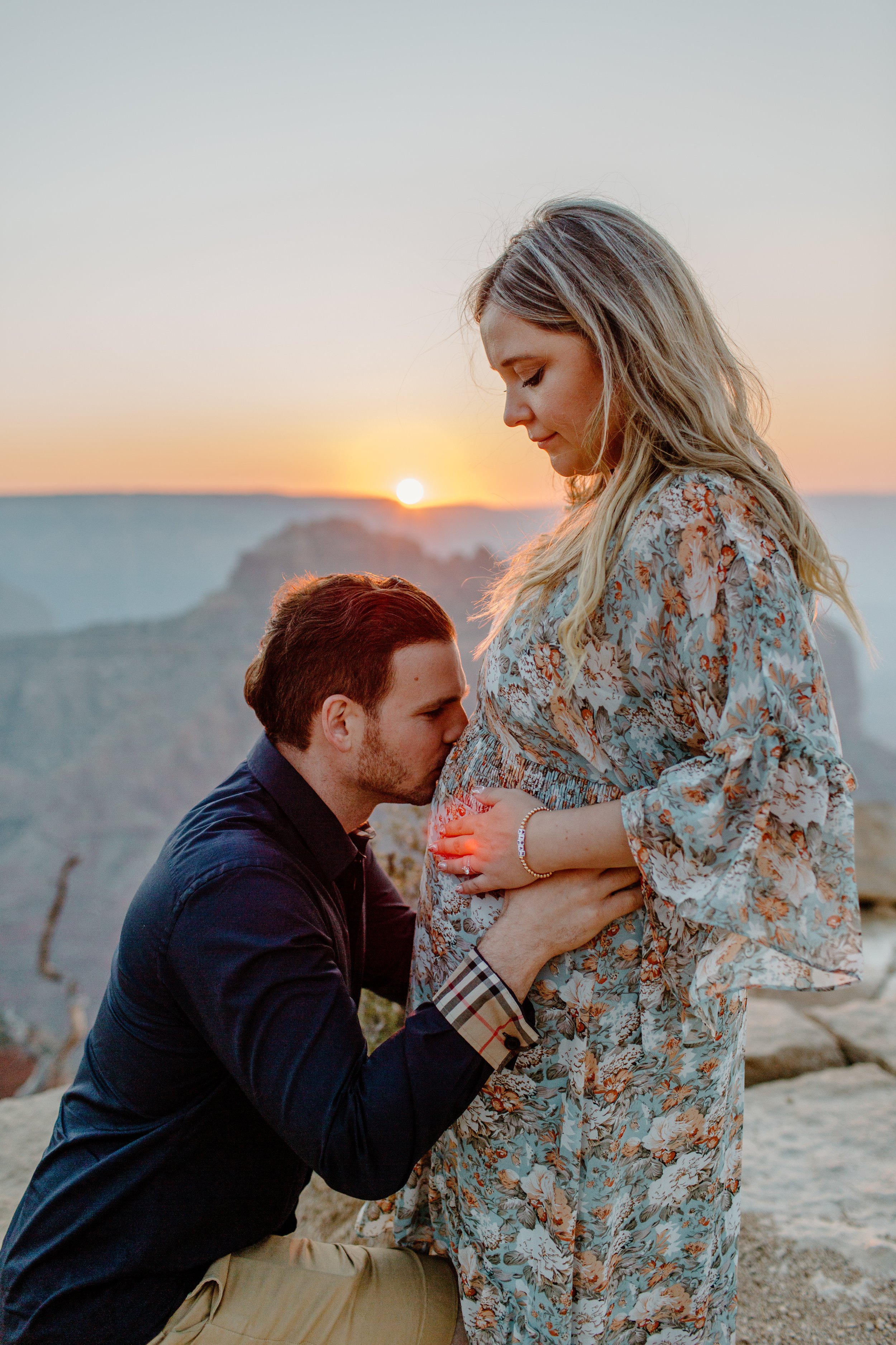  Man kisses his pregnant wife’s belly with a Grand Canyon sunset in the background 