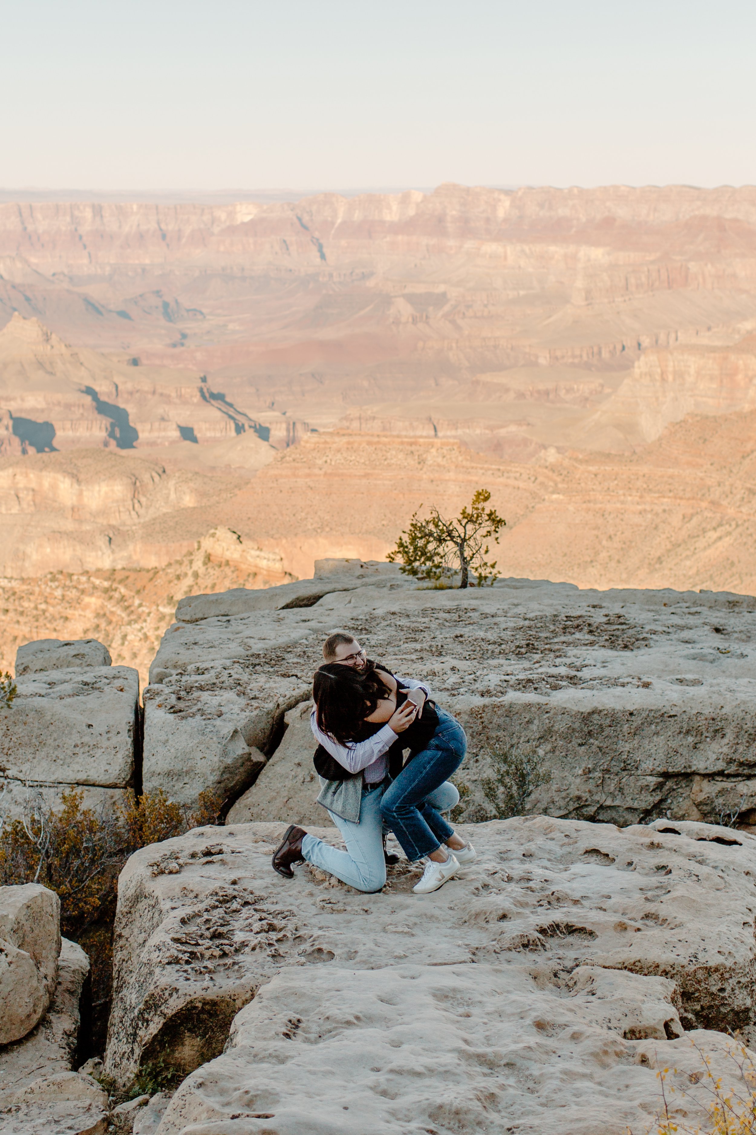  Woman hugs her fiance while he is still on one knee after proposing at the edge of the Grand Canyon 