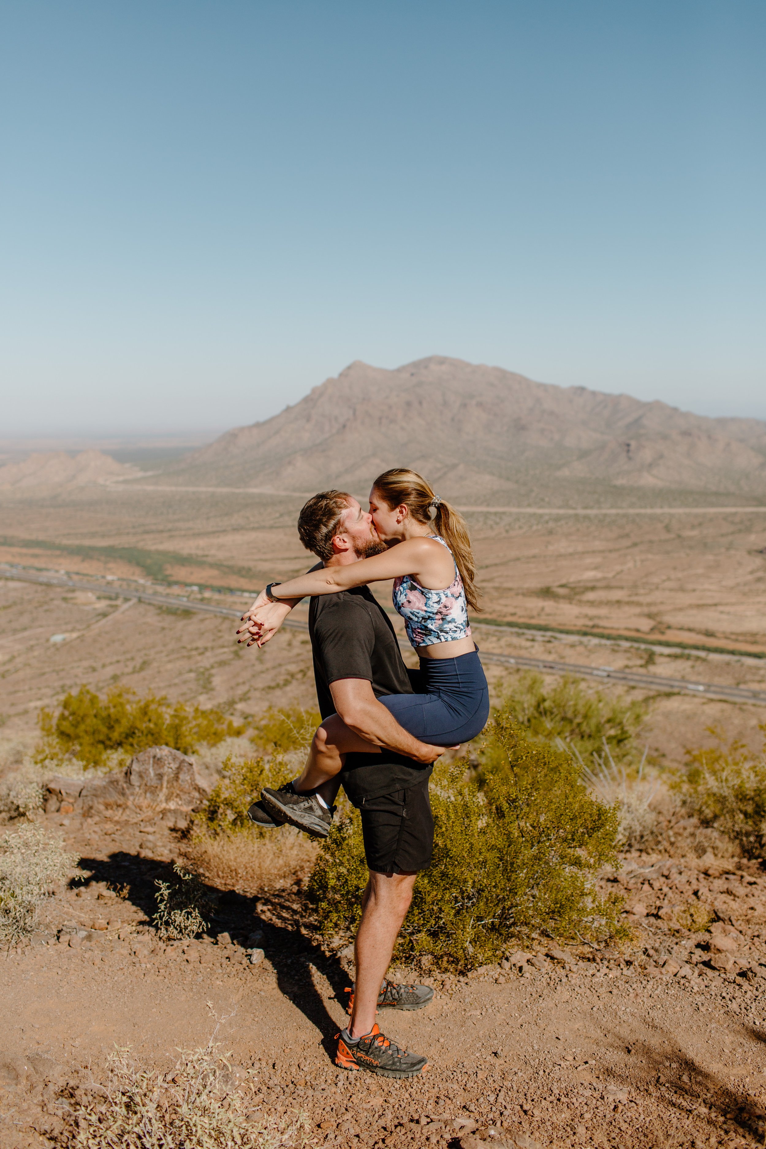  Man holds his fiance in a hug-jump at the top of Picacho Peak in Arizona 