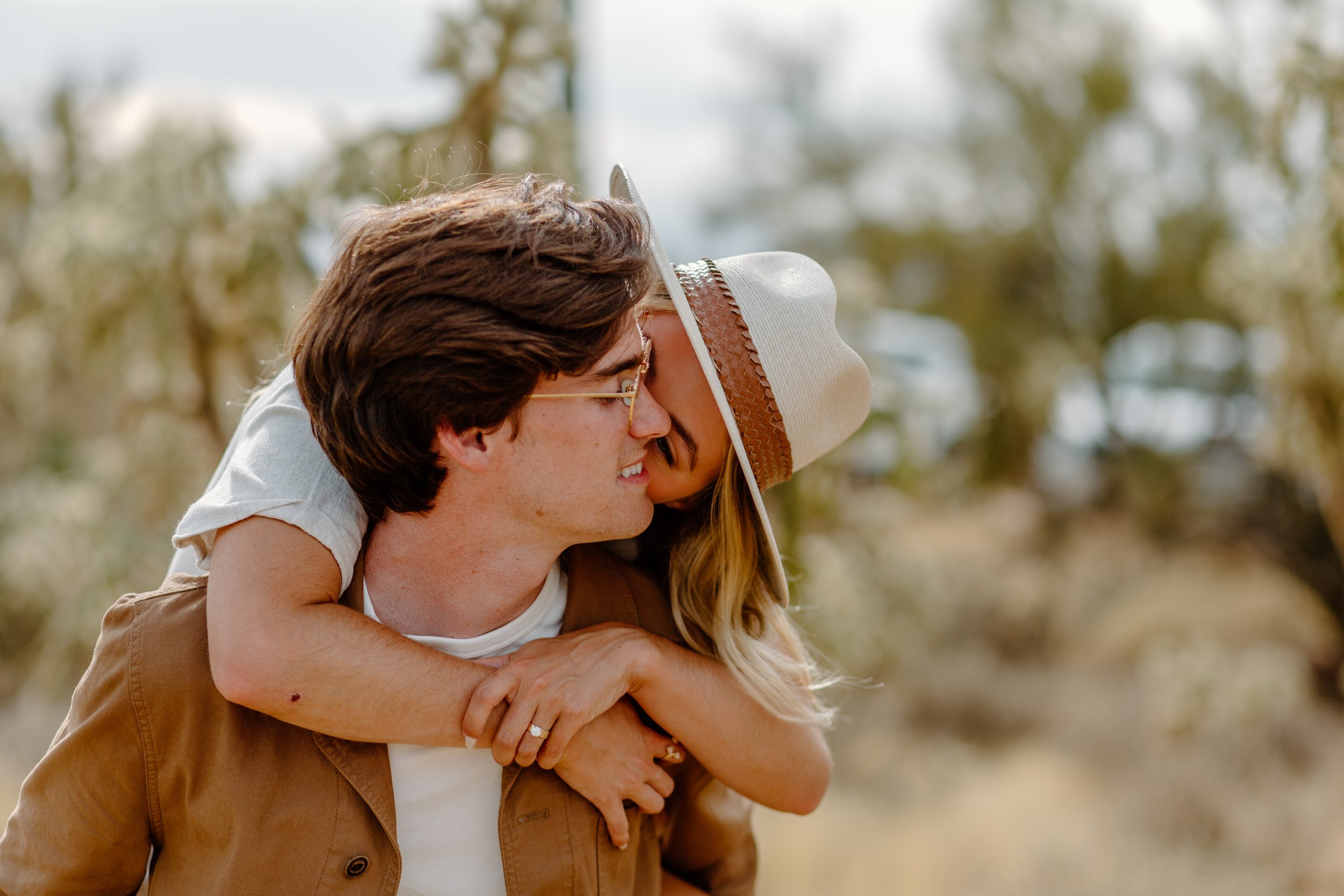  Woman kisses her boyfriend’s cheek while on his back in a desert setting in Tucson Arizona 