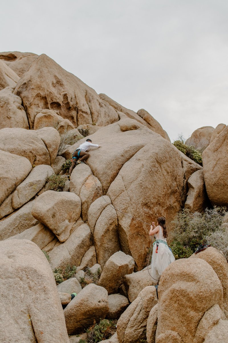  Elopement bride belays as groom climbs a rock formation in Joshua Tree National Park in California 