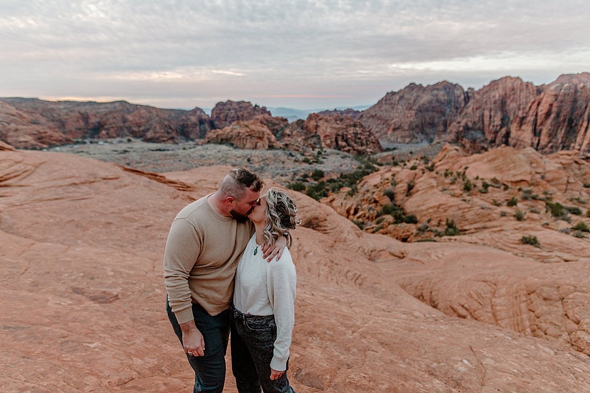  engaged man and woman kissing with canyons behind them at sunrise  