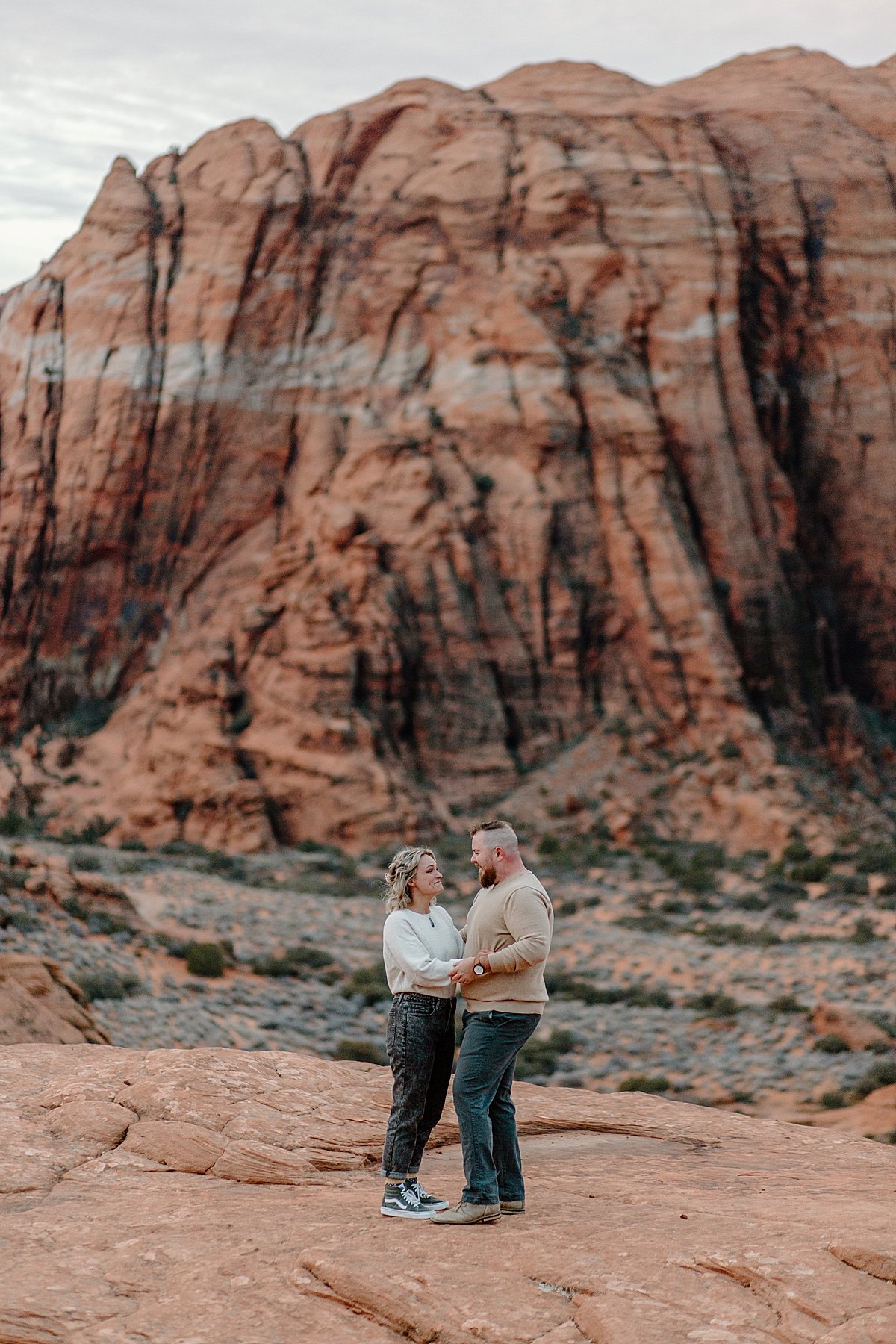  large slot canyons in Utah behind engaged couple at sunrise session 