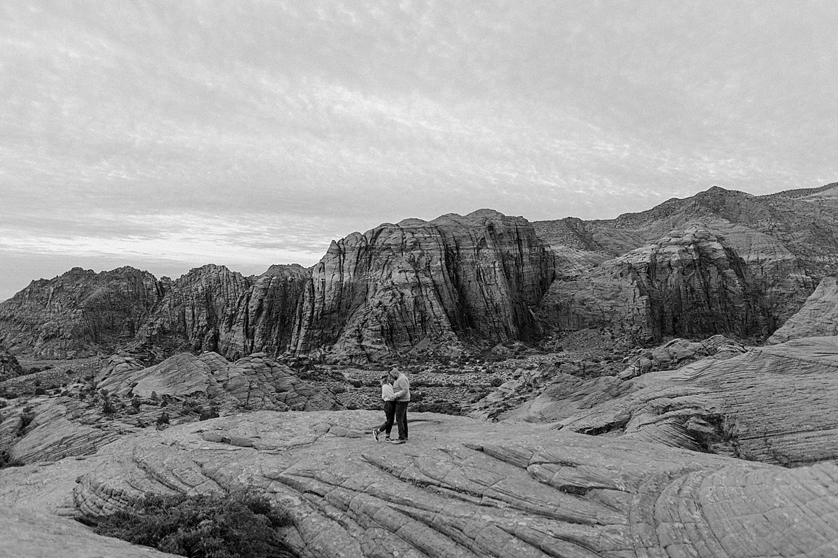  couple wearing long sleeves holding hands walking across red rocks with Arizona couples photographer  