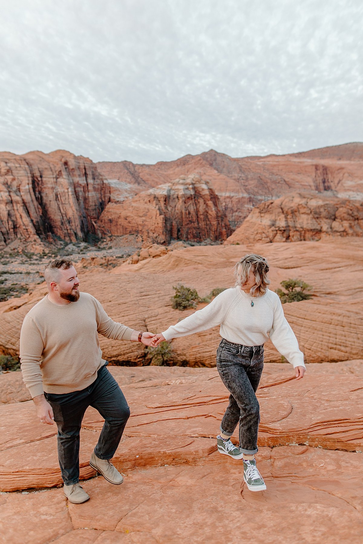  couple wearing long sleeves holding hands walking across red rocks with Arizona couples photographer  