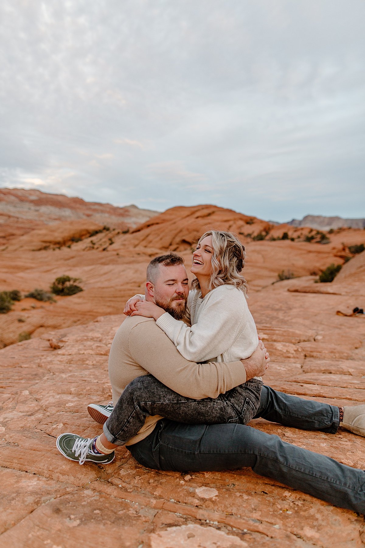  woman laughing at fiancé throughout Utah adventure session while sitting in lap of man 