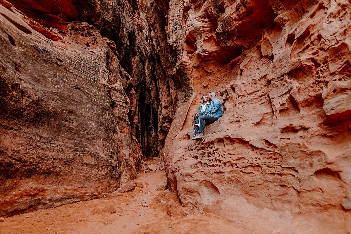  engaged couple sitting on slot canyons in Utah in jean jackets and tennis shoes 