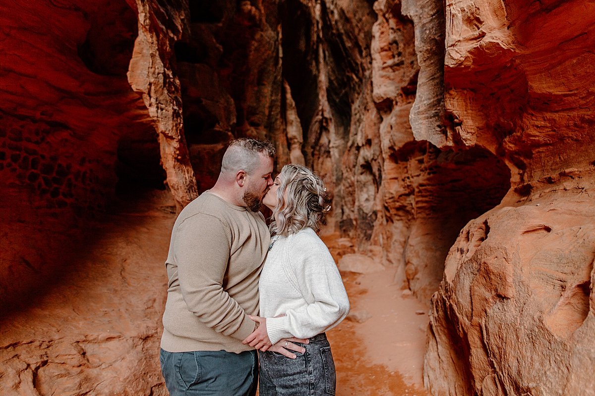  engaged couple kissing in slot canyon while holding hands 