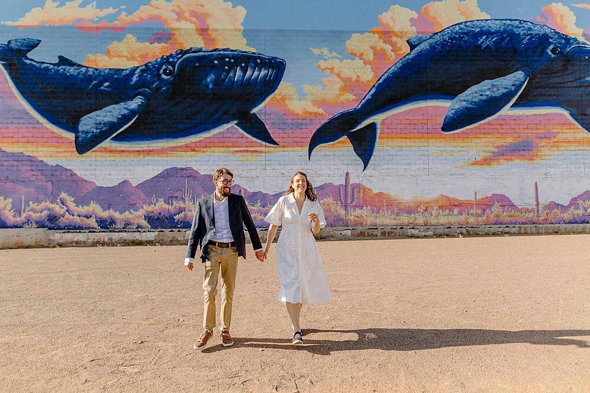  engaged couple running away from Tucson mural by Arizona couples photographer 