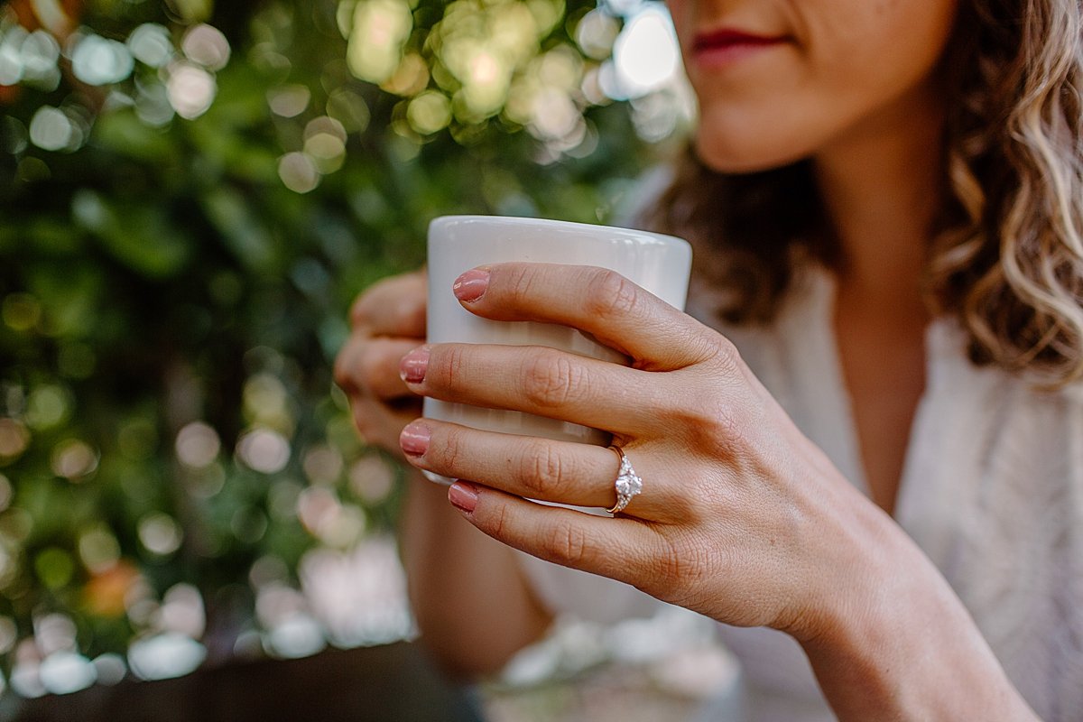  woman showing off diamond engagement ring while holding coffee cup by Arizona couples photographer 