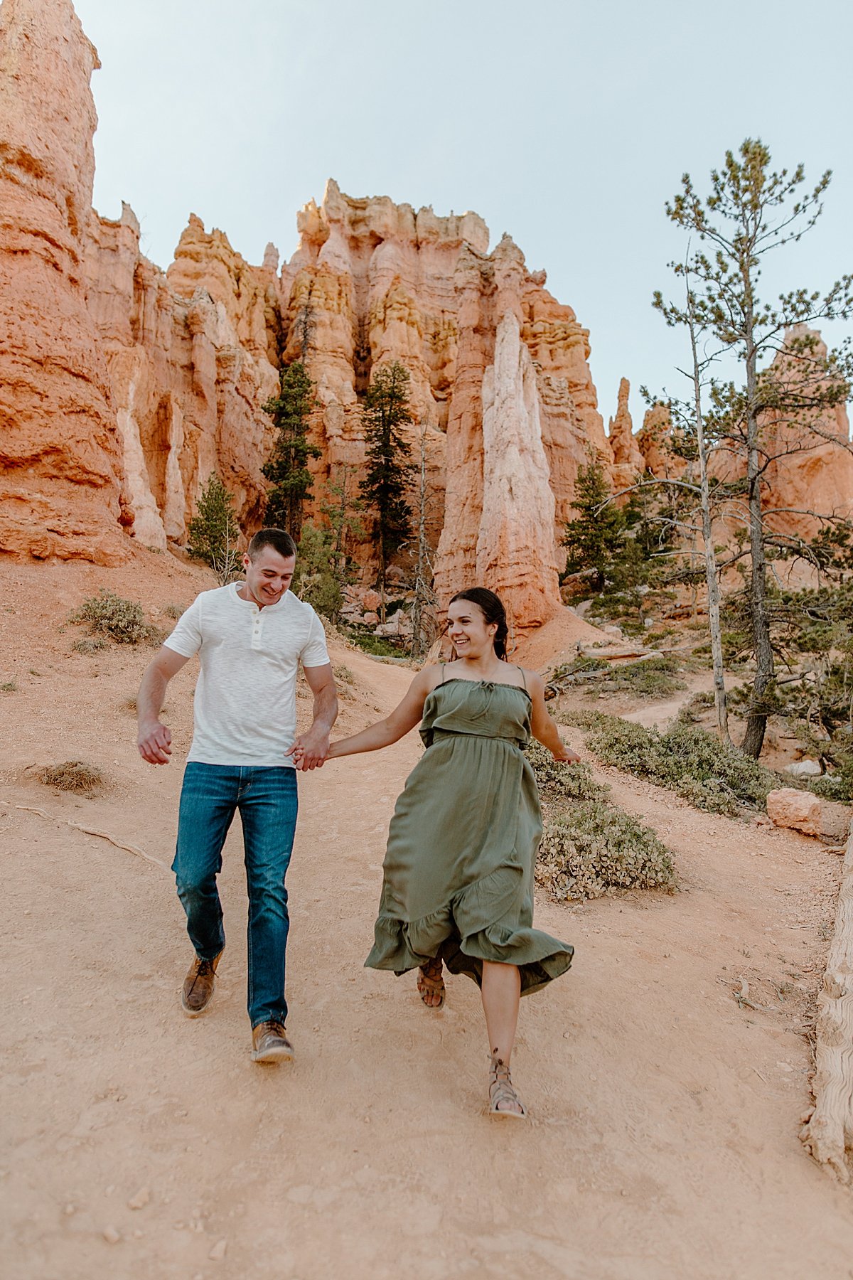  Engaged man and wife running on red rock path during Bryce Canyon adventure session 