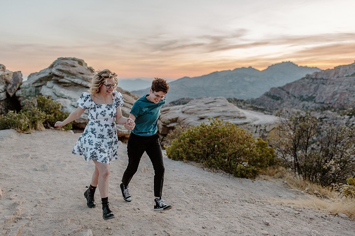  Engaged girl and girl holding hands running over rocks at Windy point 