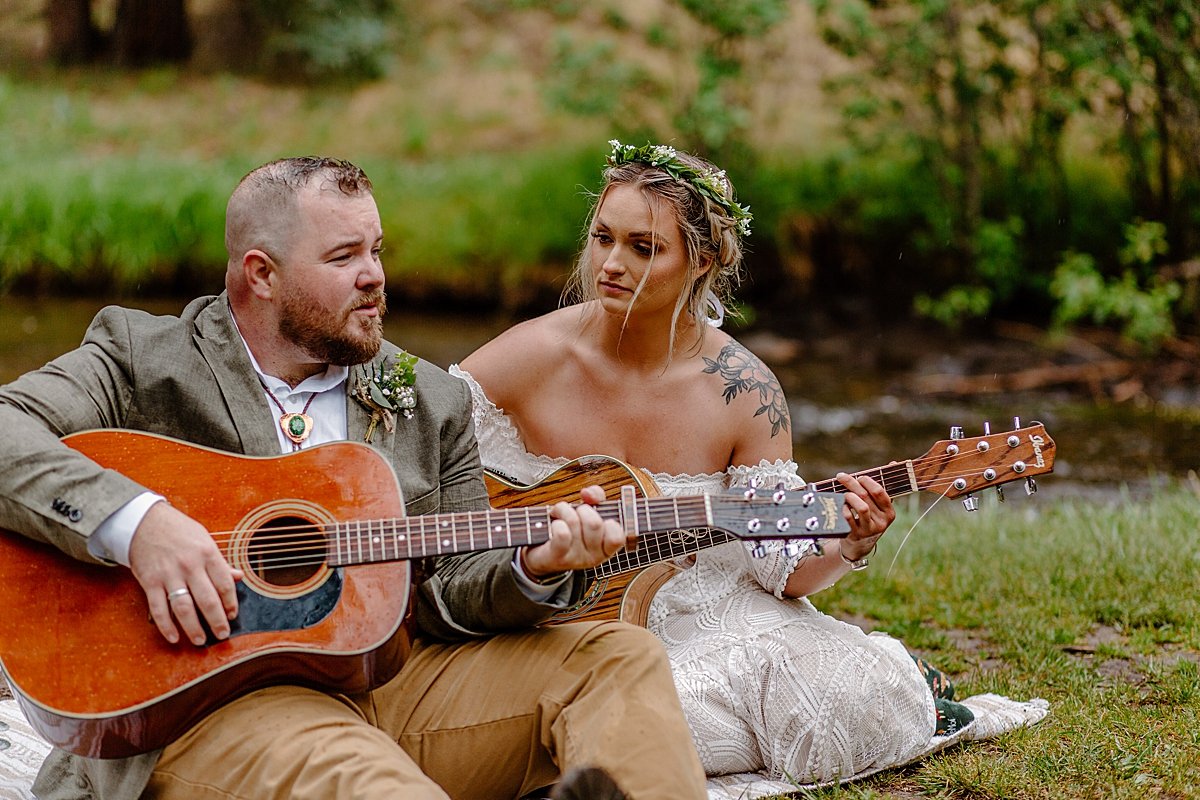  Bride and groom sitting near river playing guitar after ceremony of Greer elopement 