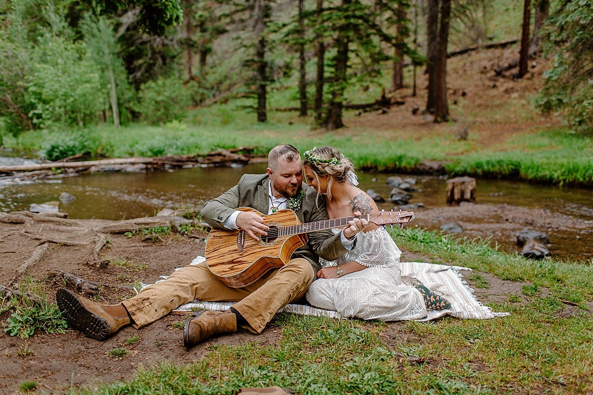  Couple sitting by River playing guitar after getting married  by Lucy Bouman 