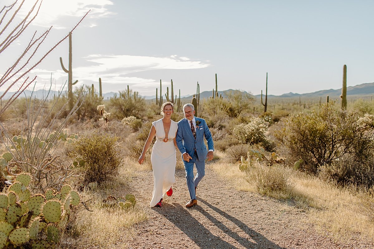  woman in gown and man in white suit walk in Saguaro National Park 