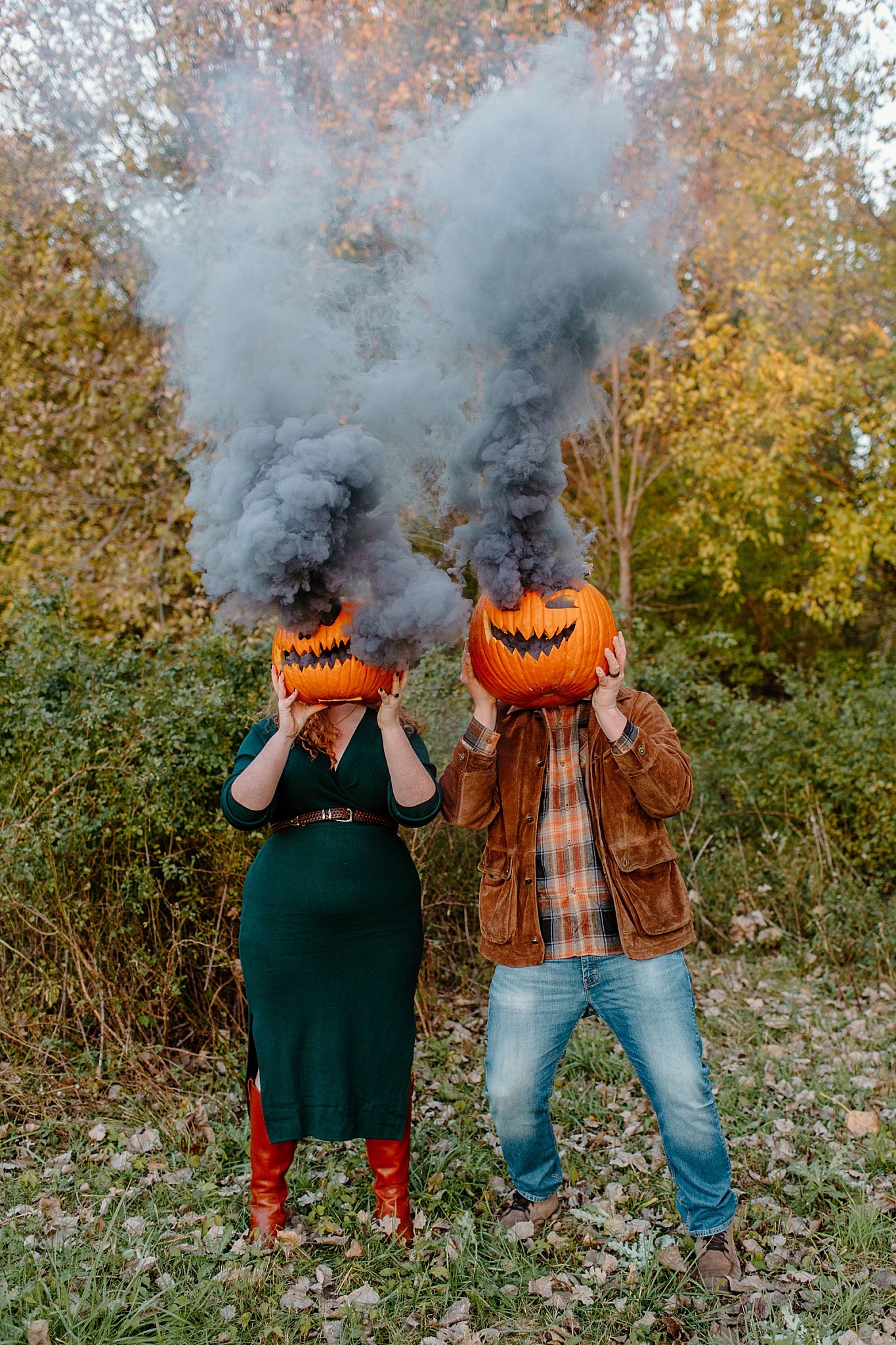  Two people stand with carved pumpkins over their heads for Halloween engagement session 